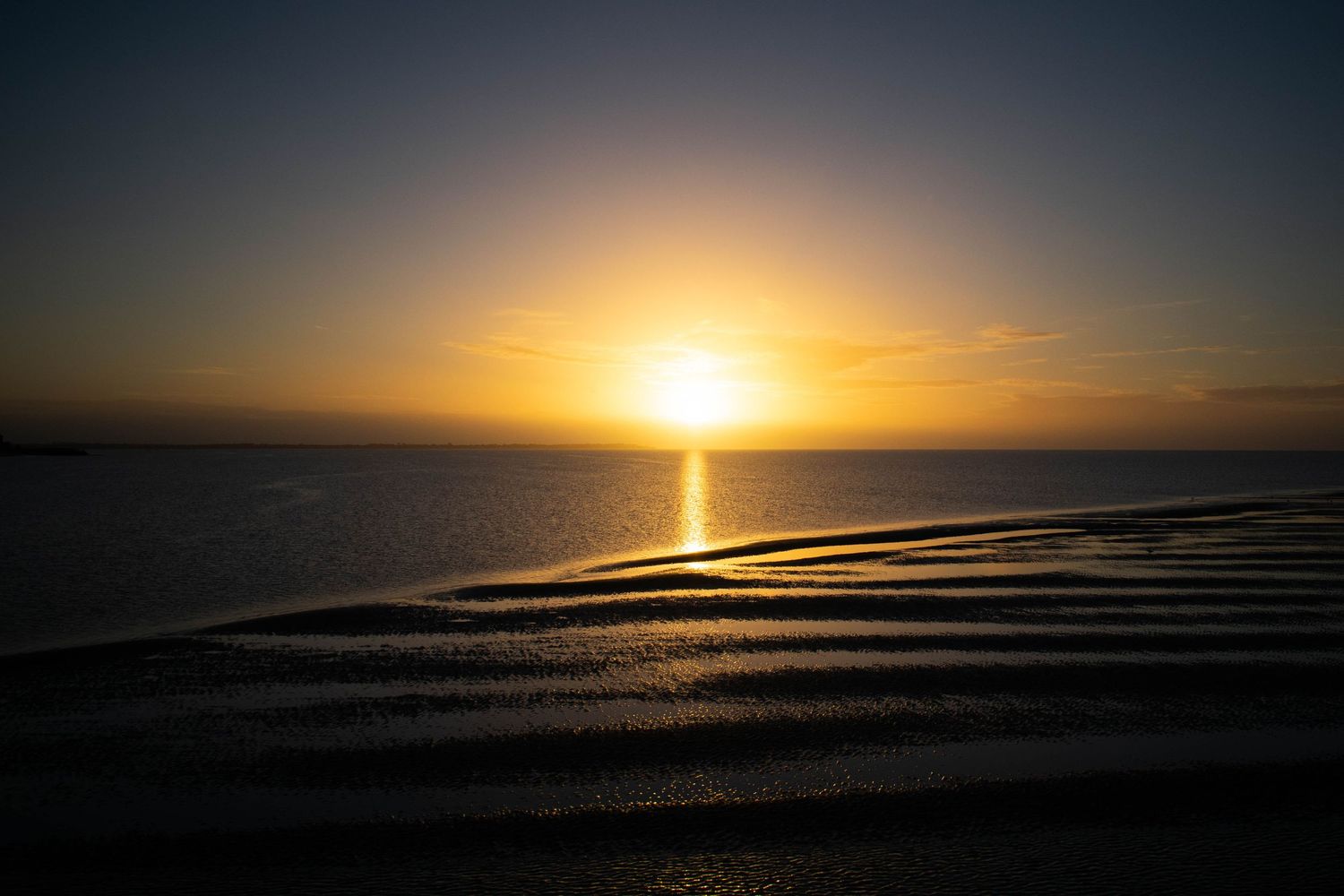 Sun setting over shallow waters with textured sand