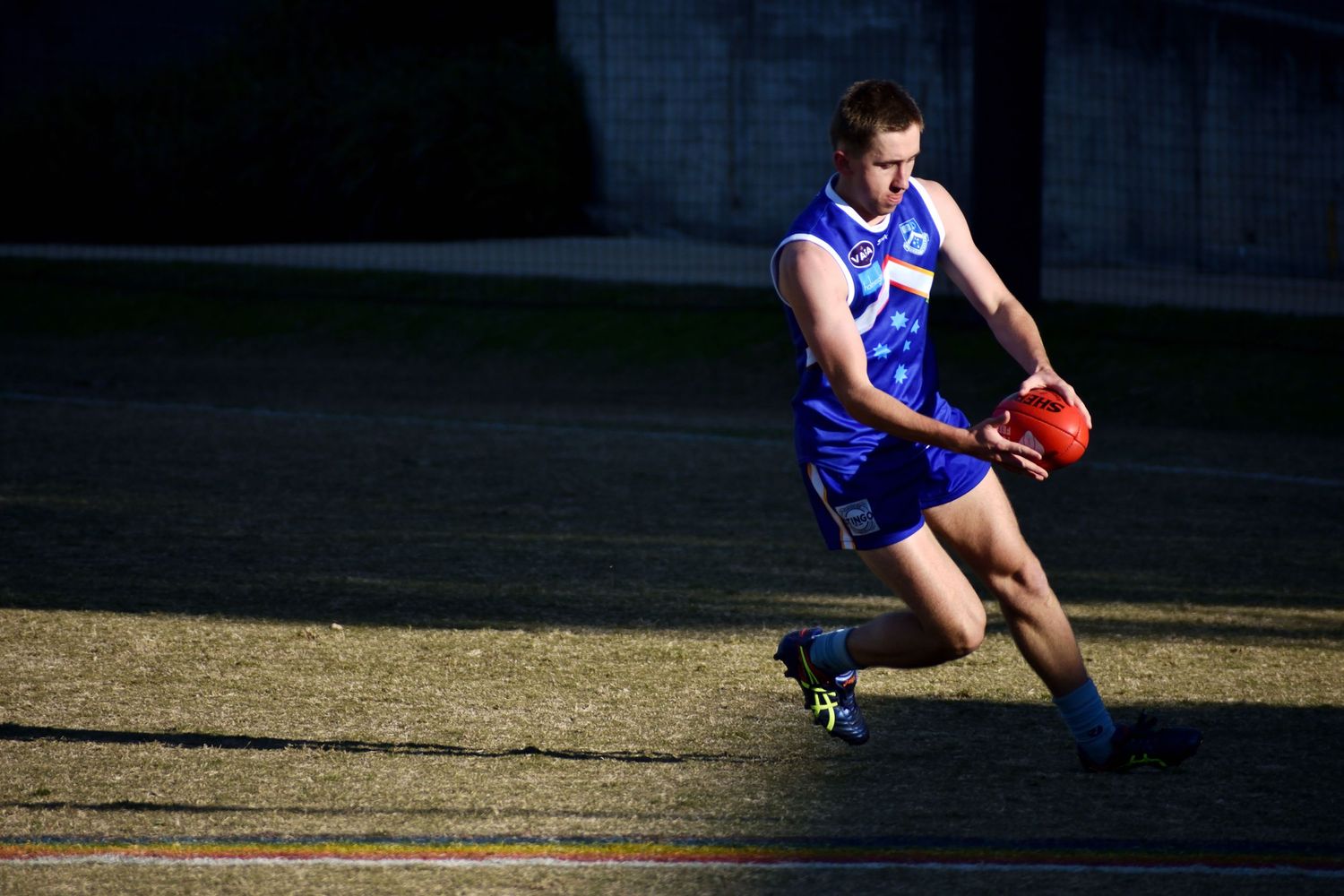 Player lining up a kick surrounded by shadows while directly being lit up - sports photography