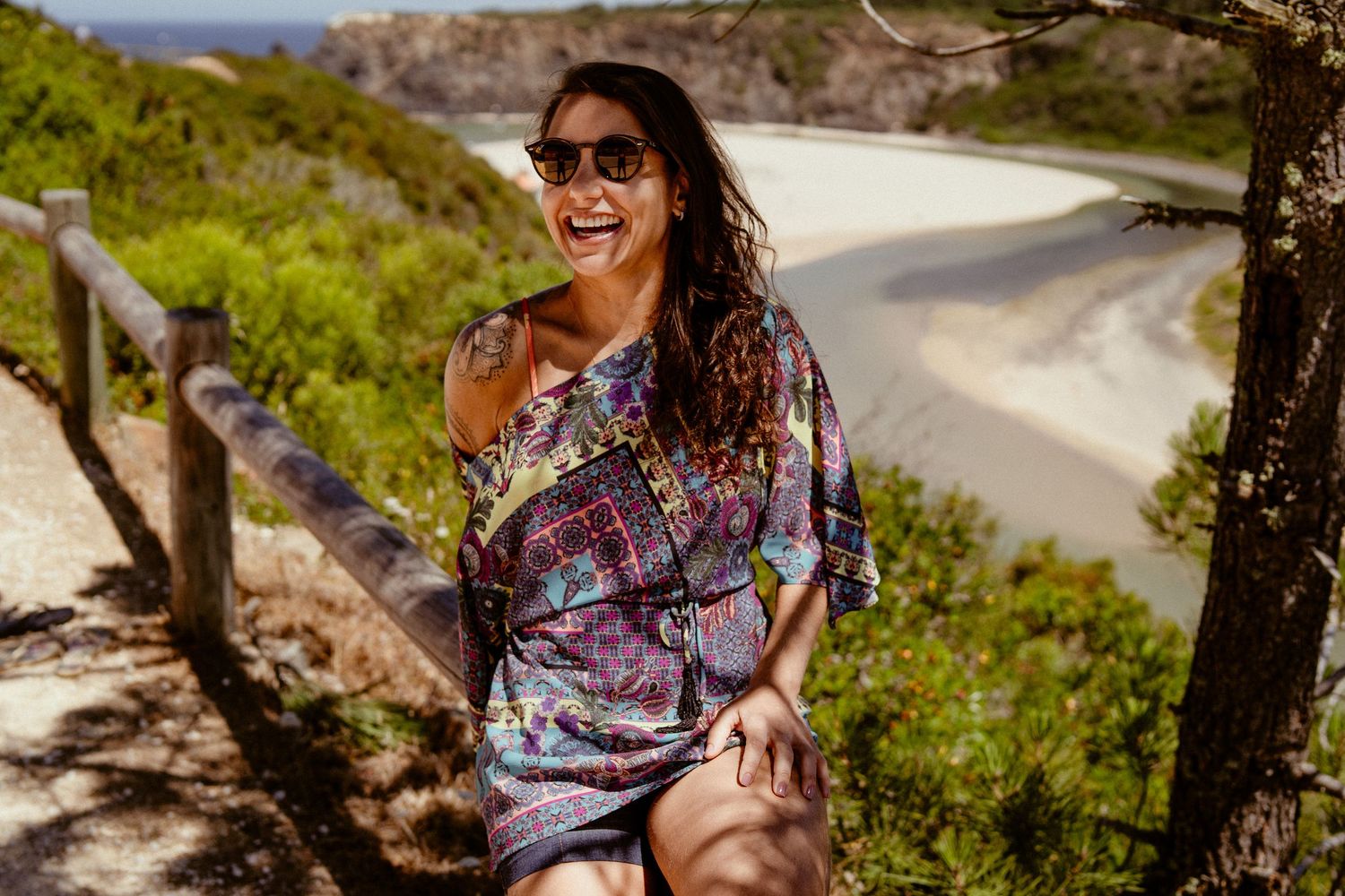 Person in colorful shirt laughing on coastal hiking trail with ocean view.