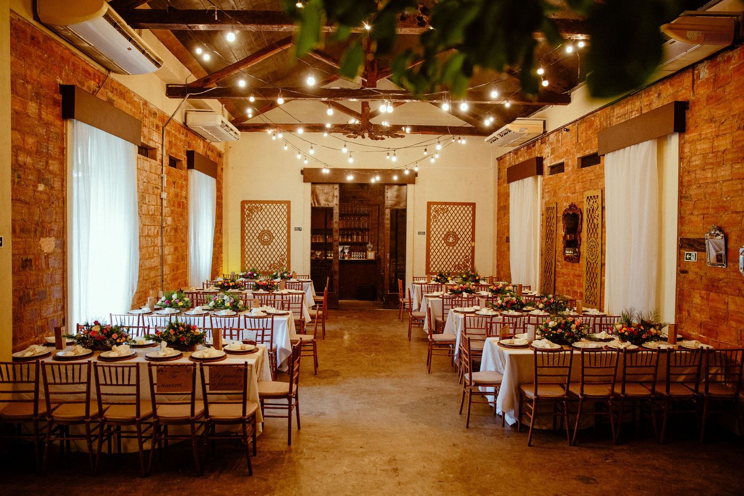 Elegant wedding reception venue with exposed brick walls, string lights and formal table settings.