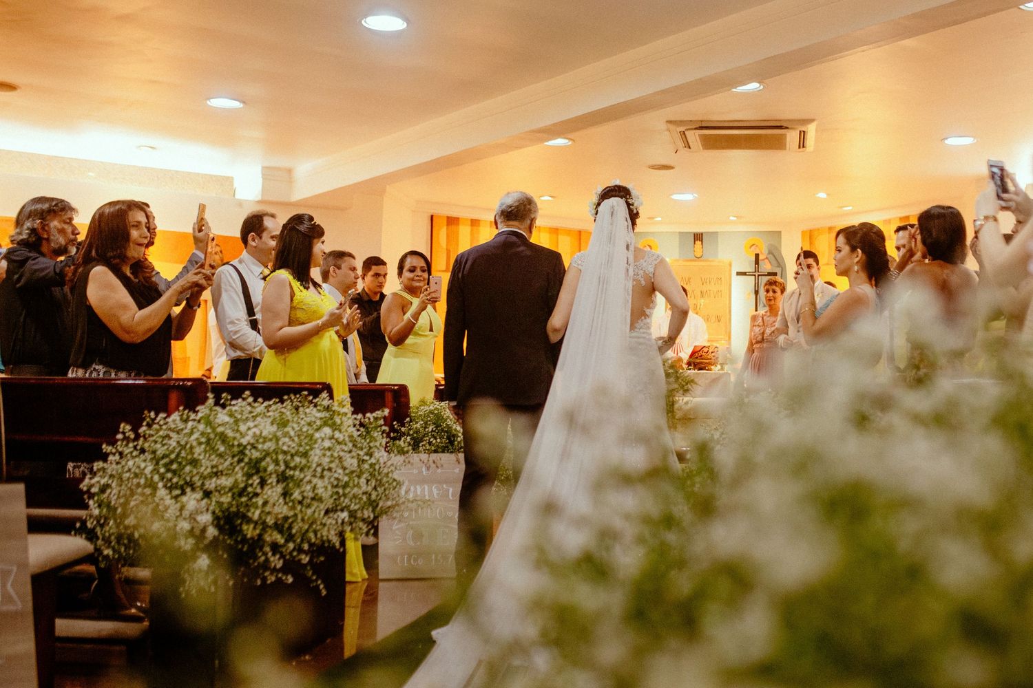 Wedding ceremony in progress with guests gathered around decorative floral arrangements in an indoor venue.