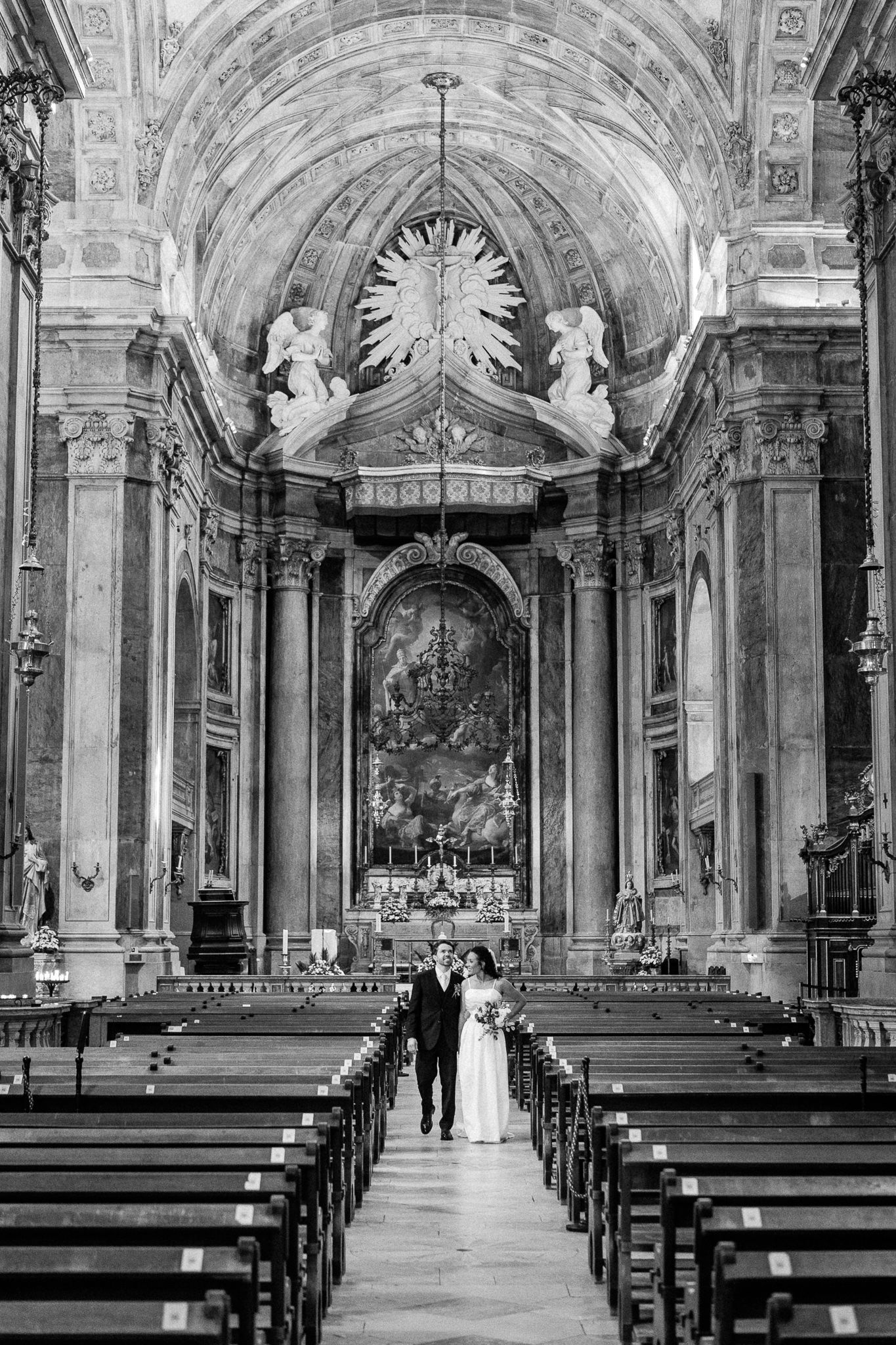 Bride and groom walking down the aisle of an ornate baroque church interior in black and white.