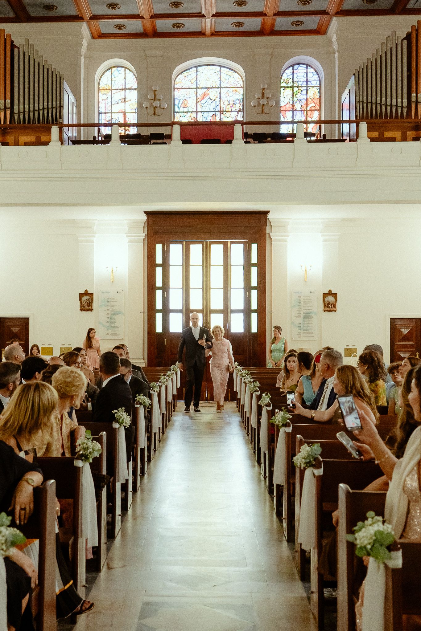 Wedding ceremony in a classic church with guests seated in wooden pews as the bride walks down the aisle.
