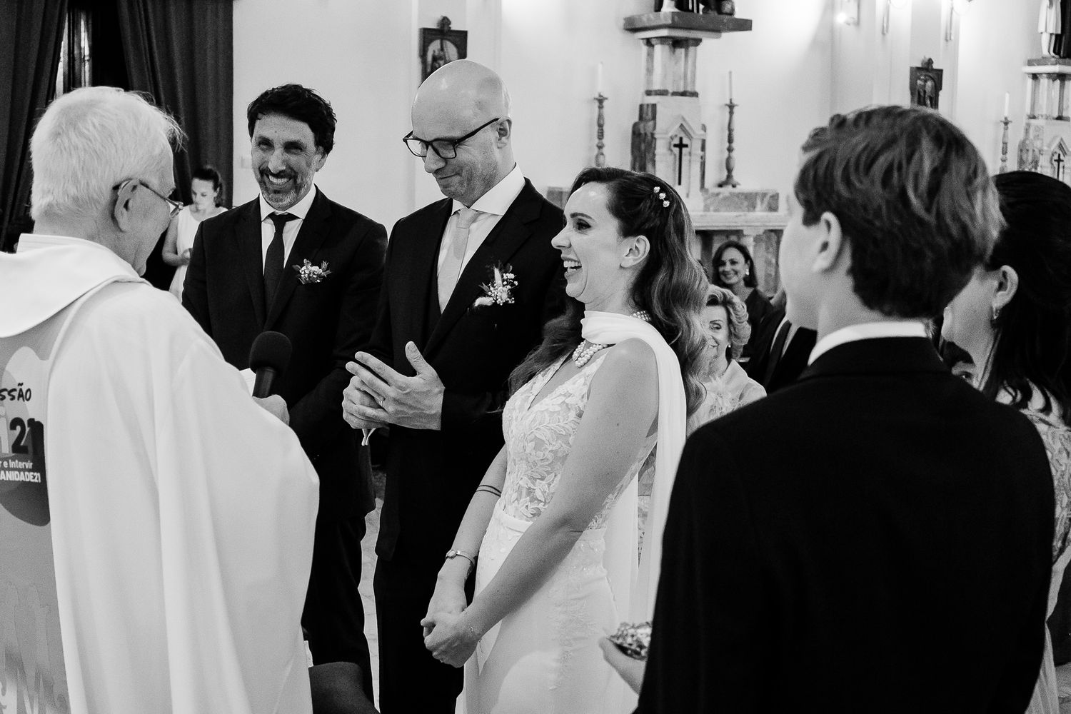 Black and white photo of a joyful wedding ceremony inside a church with bride, groom, and guests smiling.