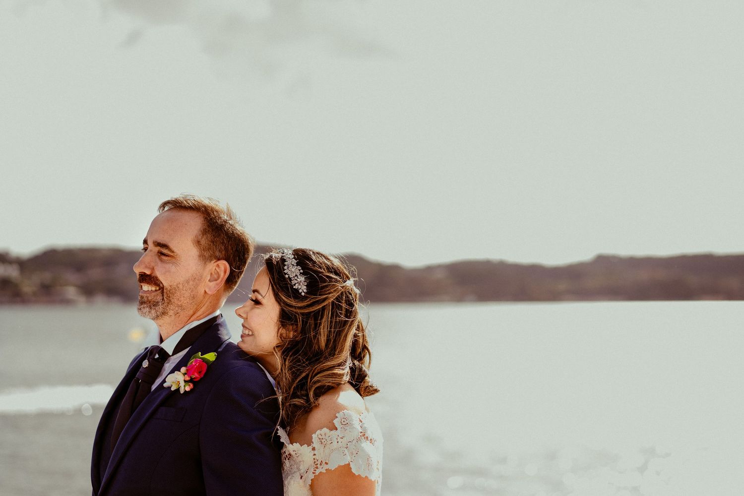 Couple shares intimate moment against waterfront backdrop during sunset wedding portraits.