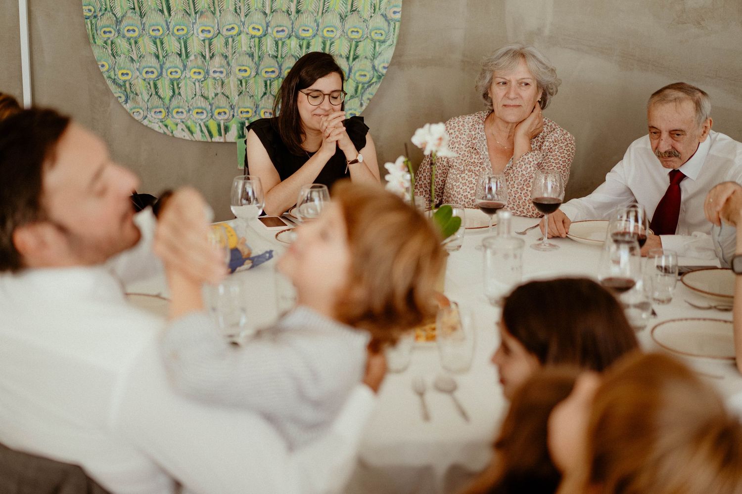 Wedding guests share laughter and conversation while seated at elegant white-clothed dining tables during a reception.