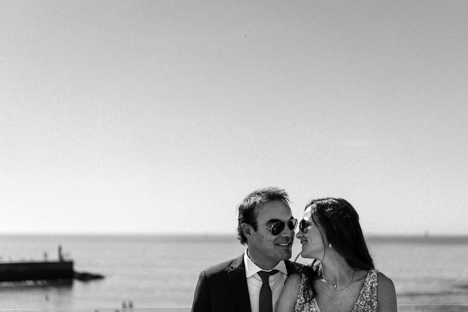 A black and white photo captures an intimate moment between a couple by the waterfront.