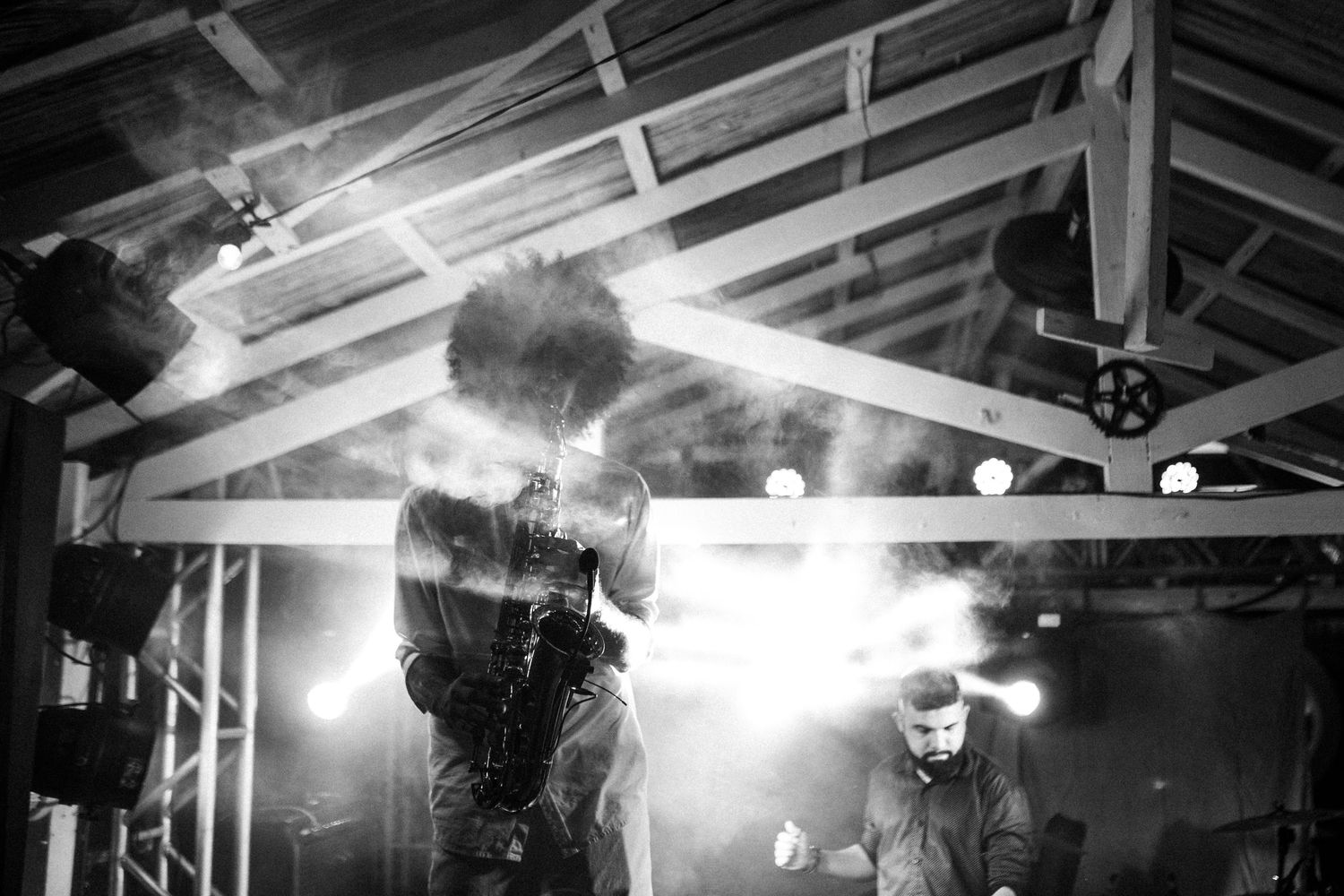 A silhouetted performer creates a dramatic effect on stage with bright backlighting and smoke effects during a live show.