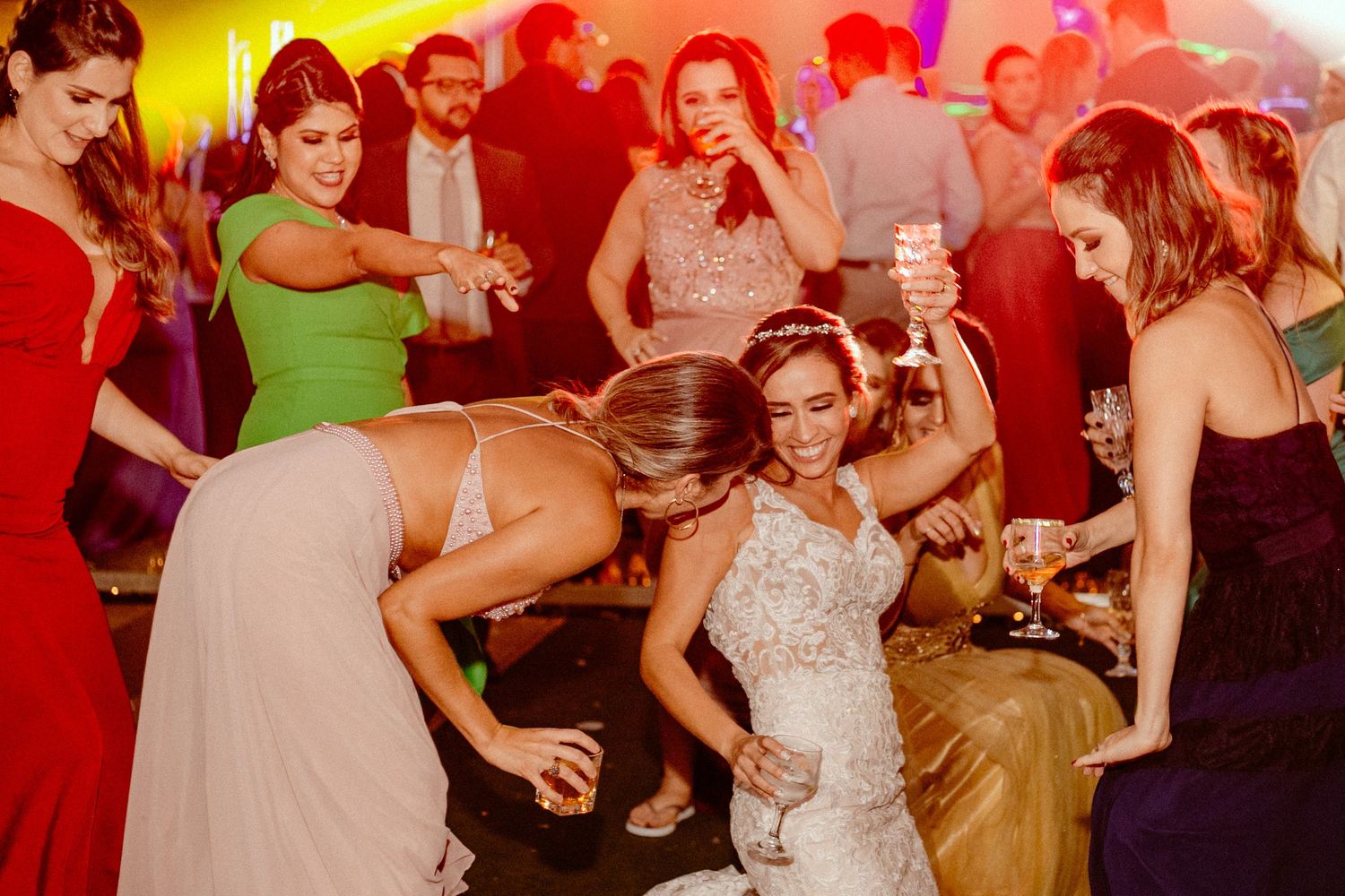 Wedding guests dance and celebrate on a colorfully lit dance floor during an energetic reception party.