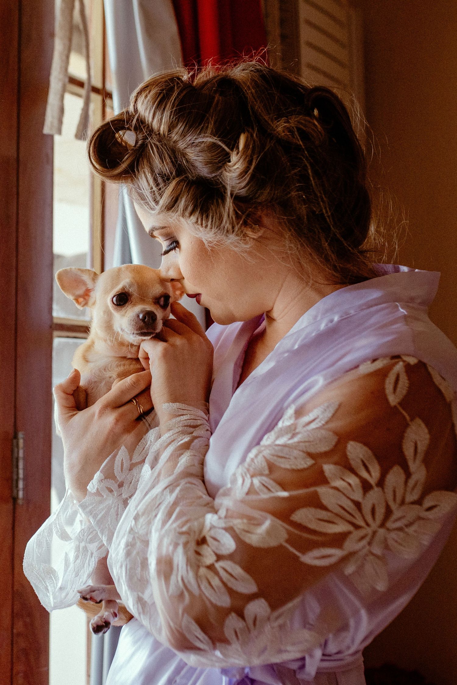 Someone in a floral robe holding and cuddling a small Chihuahua puppy by a window.