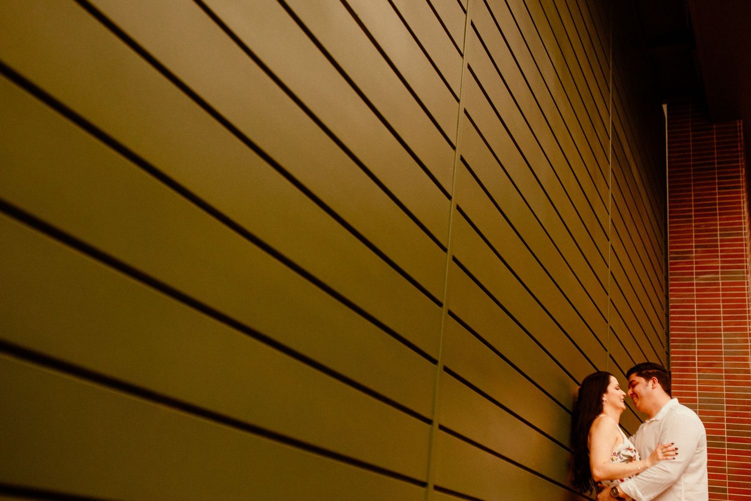 Romantic couple embracing in a dimly lit corner with dramatic shadows and lines on yellow wall.