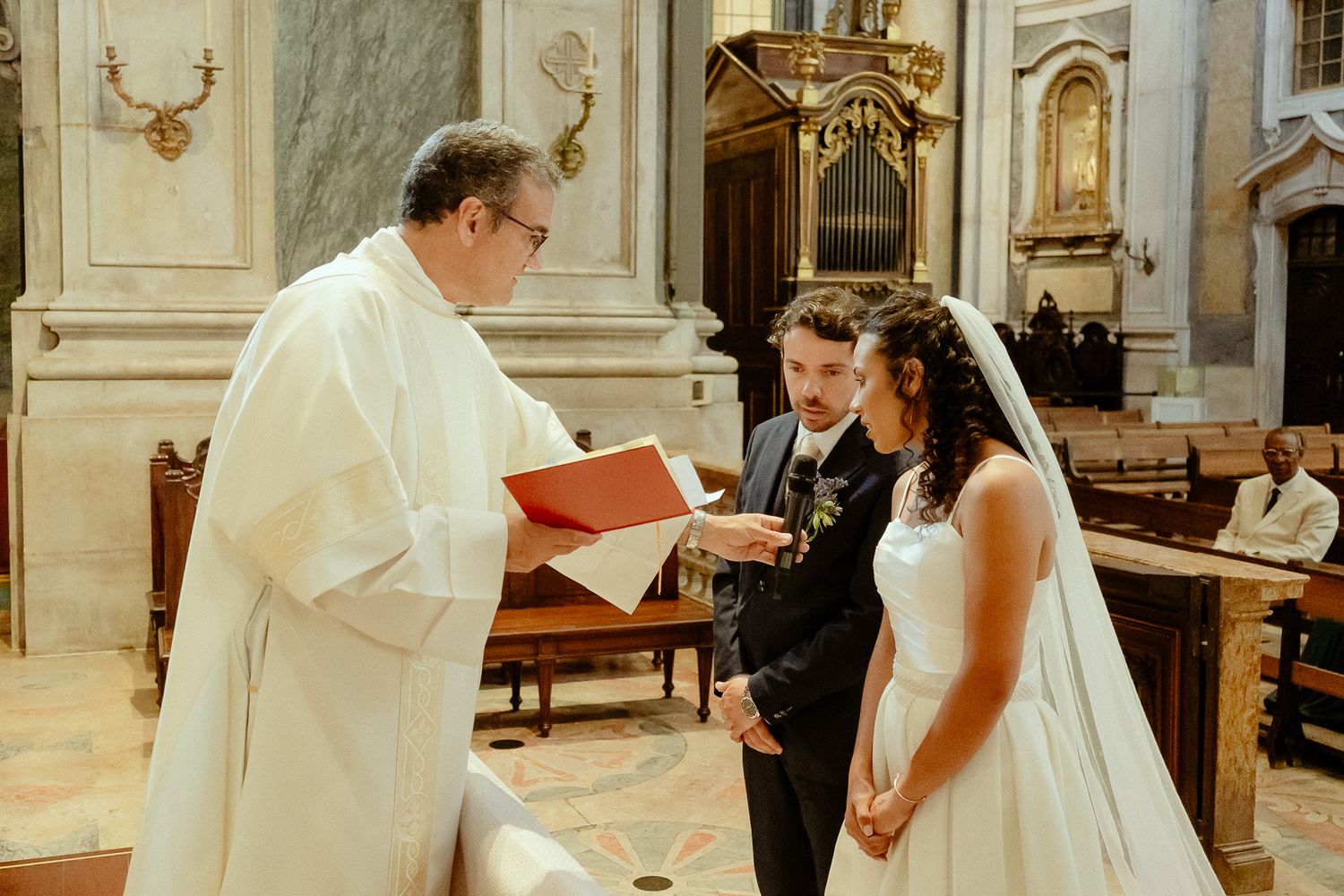 A couple exchanges wedding vows before a priest in an elegant church during a traditional Catholic wedding ceremony.