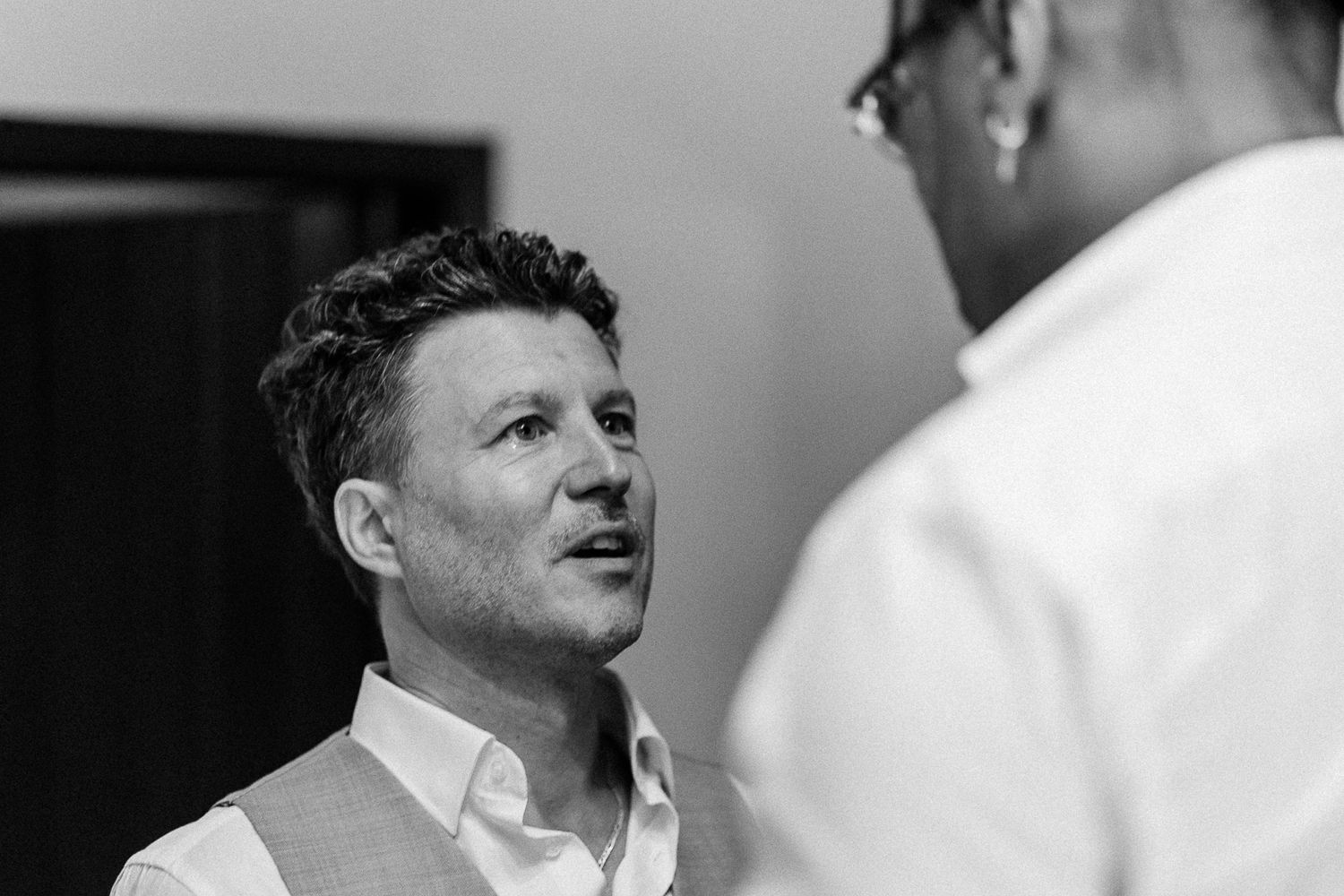 Black and white photo of two men in formal attire having a conversation at an indoor event.