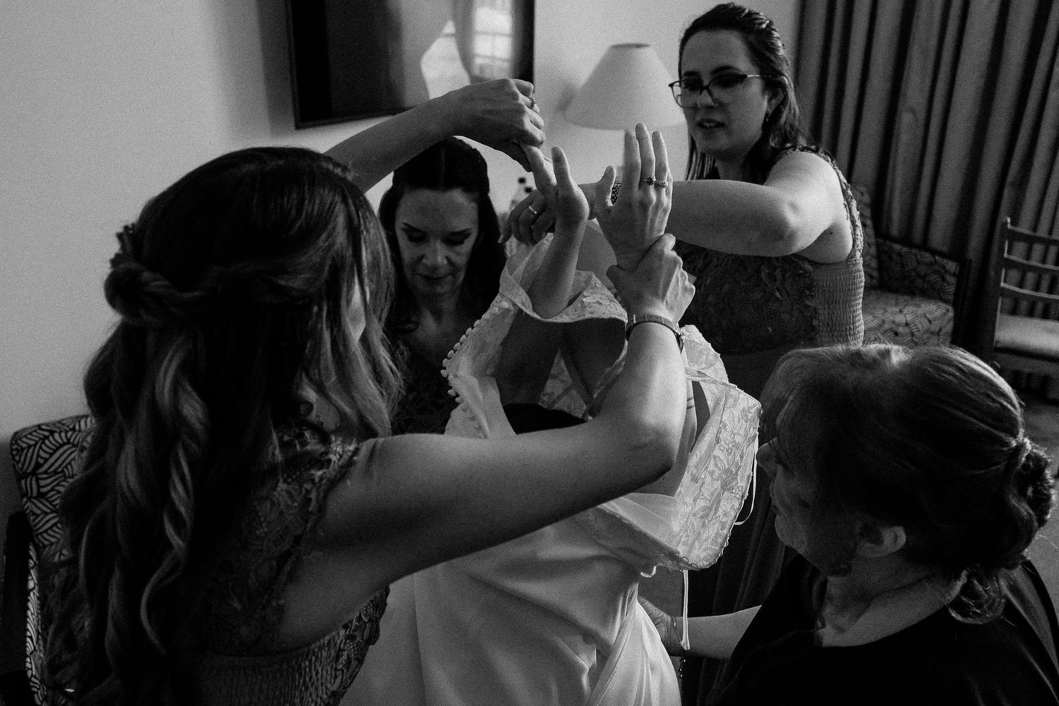 Black and white photo of bridesmaids helping bride get dressed before wedding ceremony.