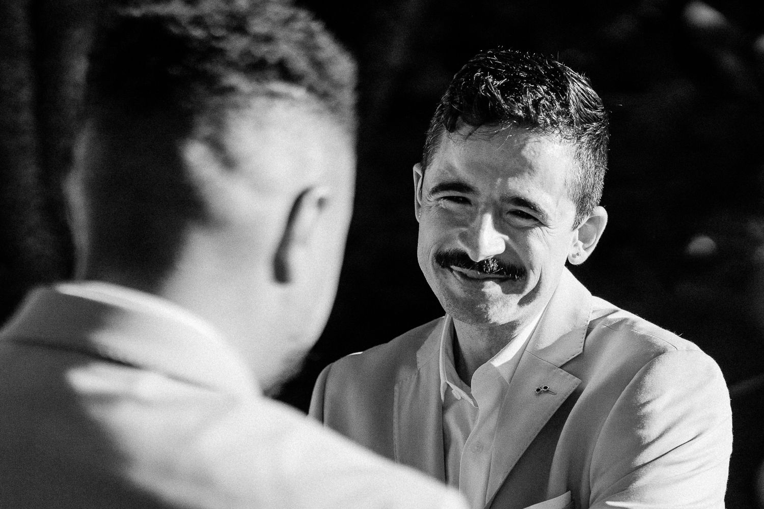 Black and white photo of a smiling man with mustache in a suit jacket at a formal event.