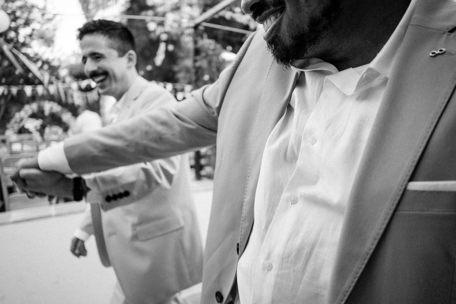 Black and white photo of two men in suits at a wedding, one smiling and adjusting the other's jacket.