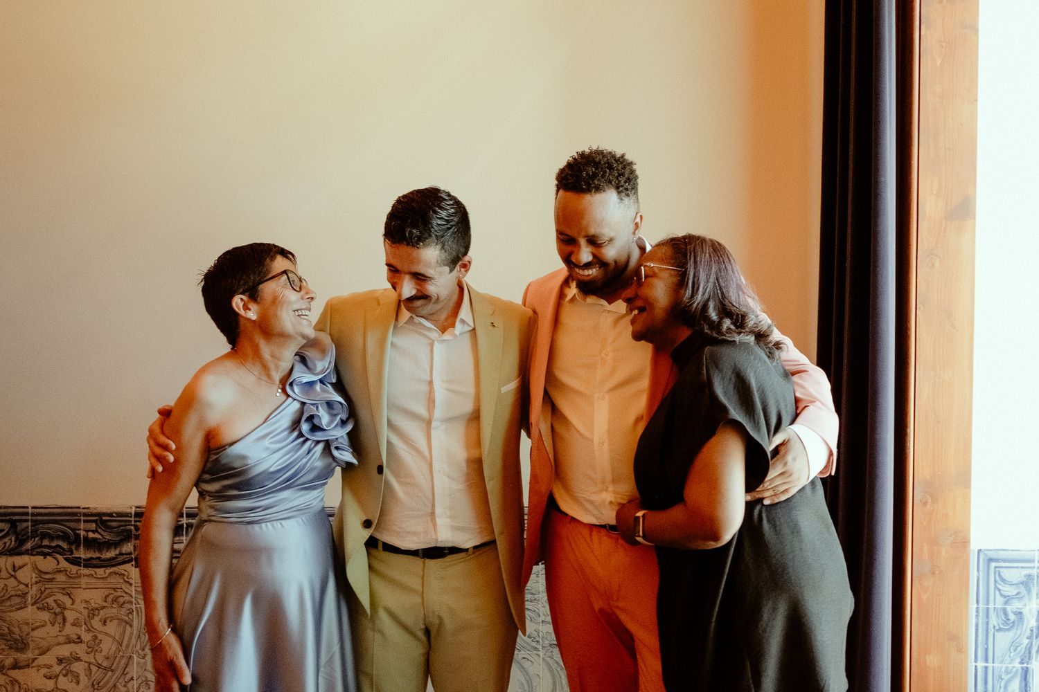 Four friends smiling and embracing together indoors, dressed in elegant formal attire for a special occasion.