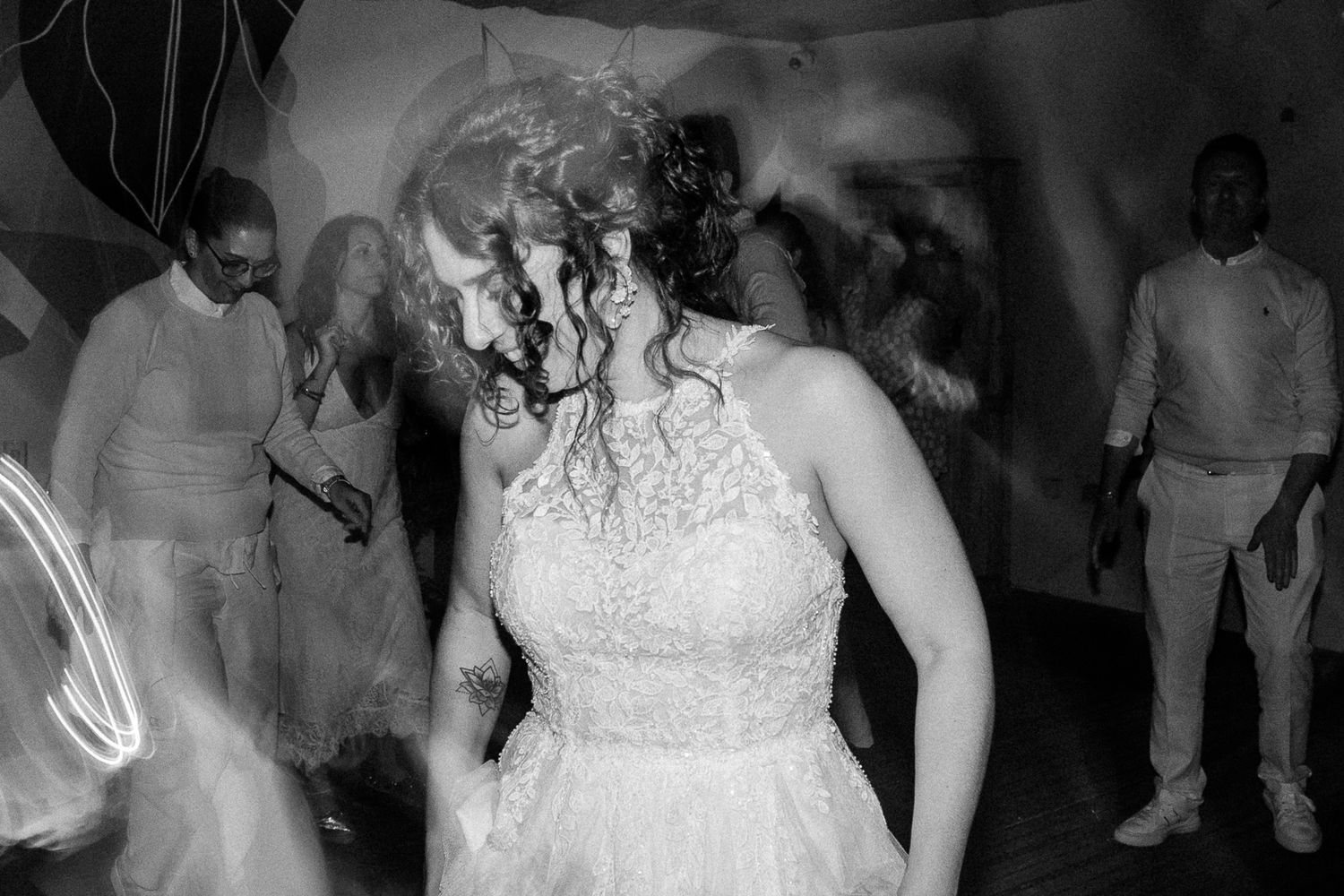 Bride in lace wedding dress dancing joyfully with guests at a lively wedding reception in black and white.