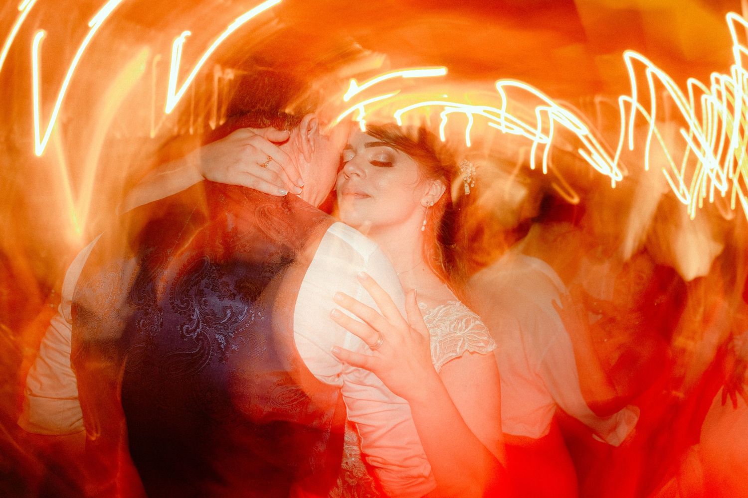 A bright orange motion blur image showing silhouettes of performers or dancers in dark clothing against a glowing background.