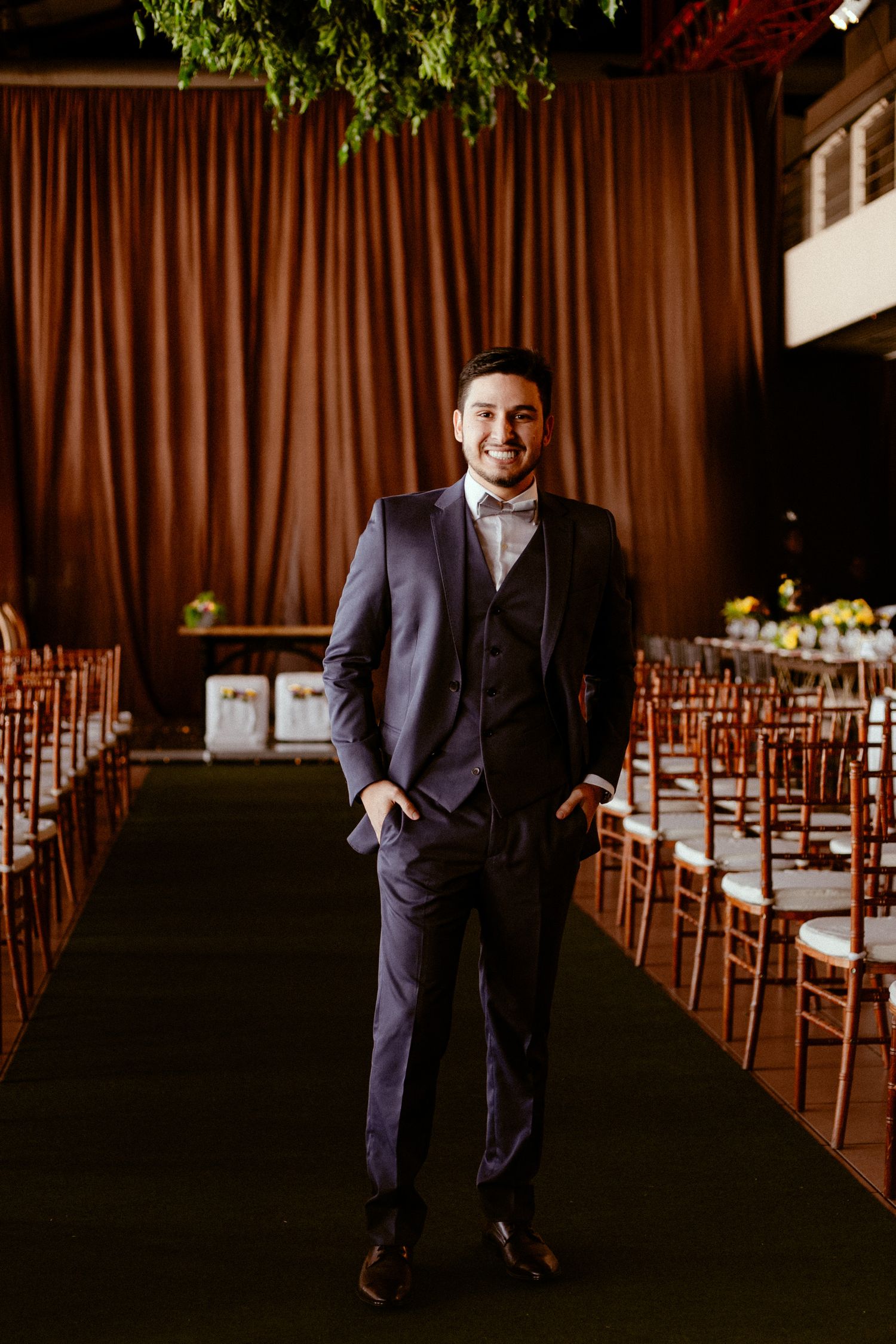 Four connected photos showing someone in a dark navy suit walking and posing in an indoor venue with wooden chairs.