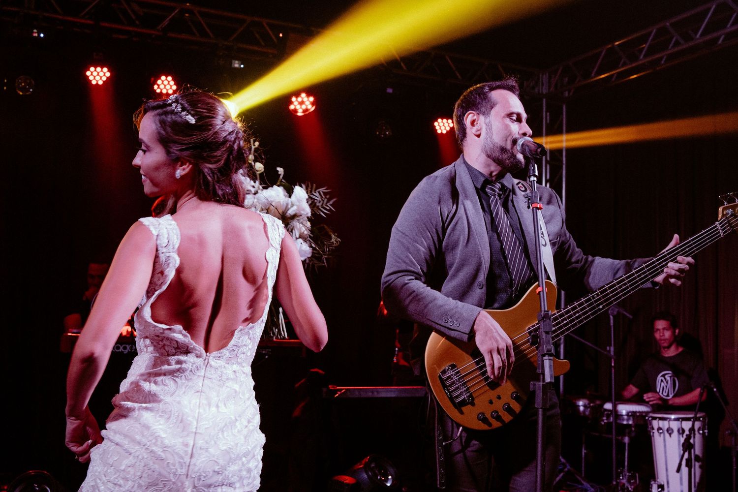 Musicians perform on stage with dramatic yellow lighting at a live concert venue.
