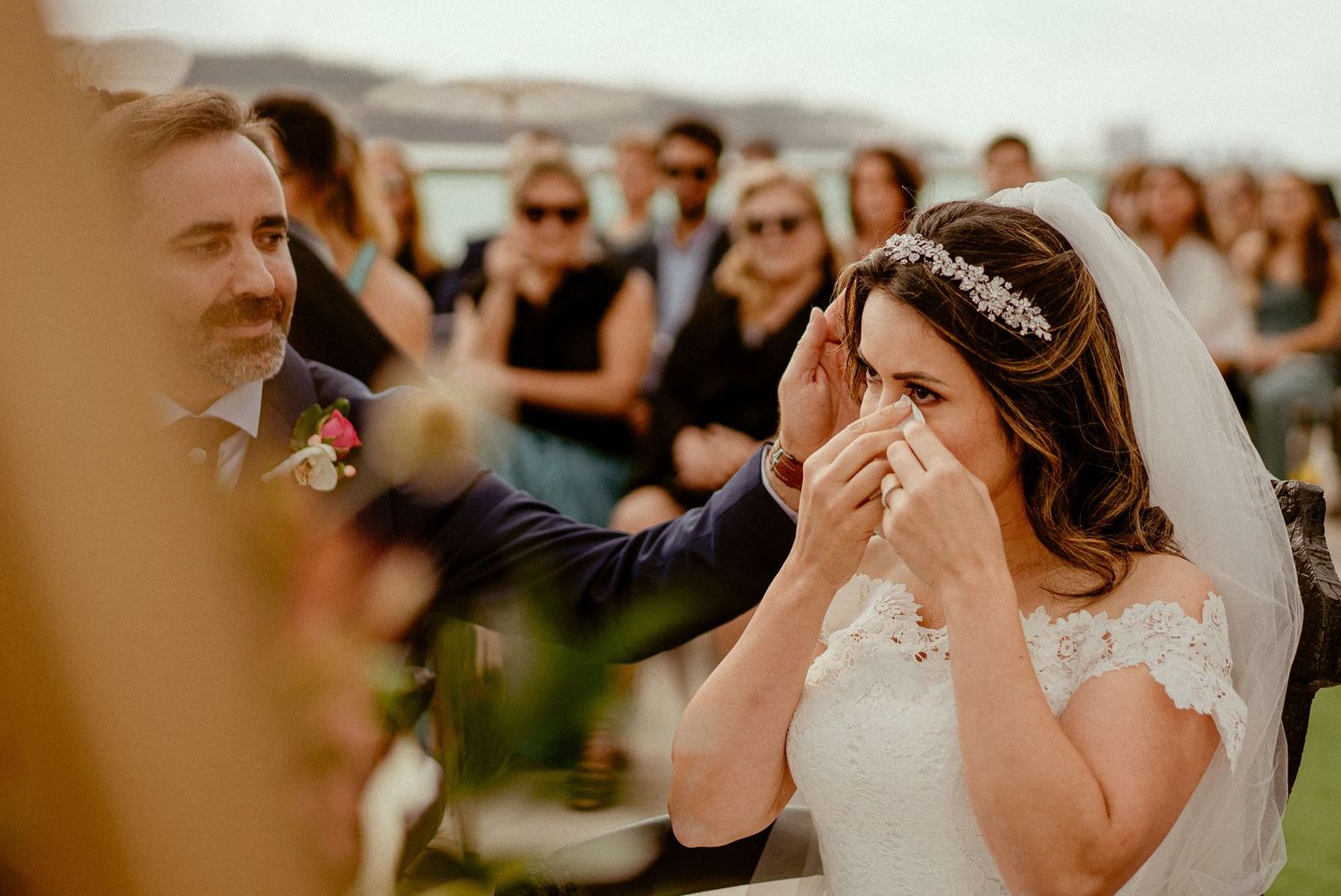 Bride becomes emotional during outdoor wedding ceremony while wearing lace dress and crystal headpiece.