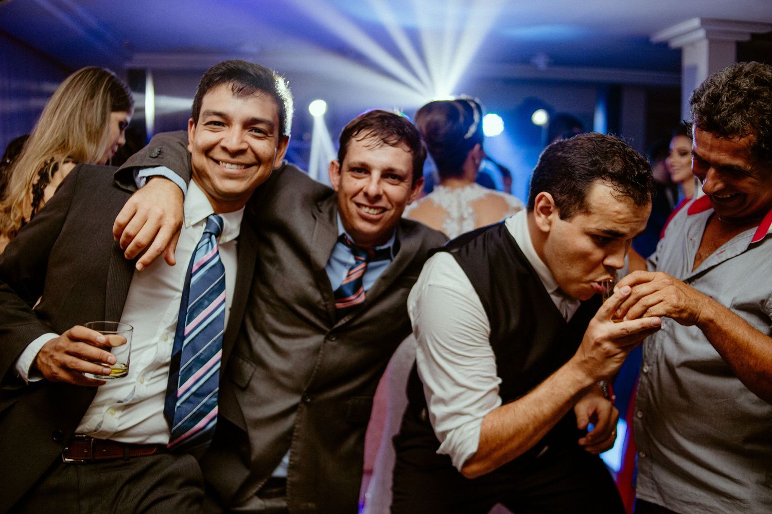 Wedding guests having fun and laughing together on the dance floor with blue lighting in the background.