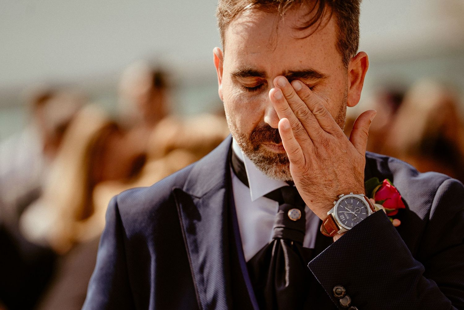 Close-up of emotional moment during wedding ceremony with navy suit and red boutonniere.