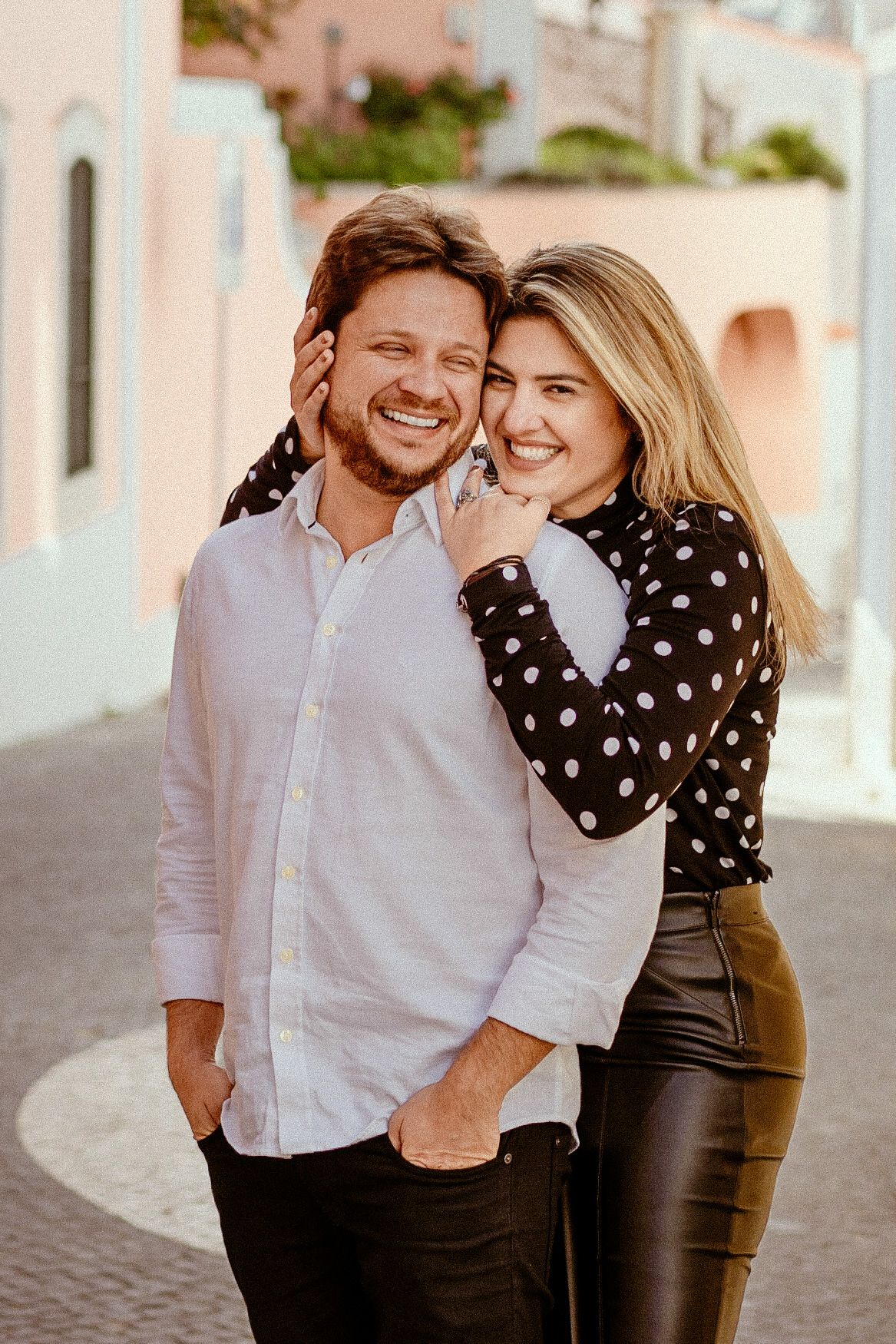 Romantic couple sharing a tender moment on a sun-lit Mediterranean street.