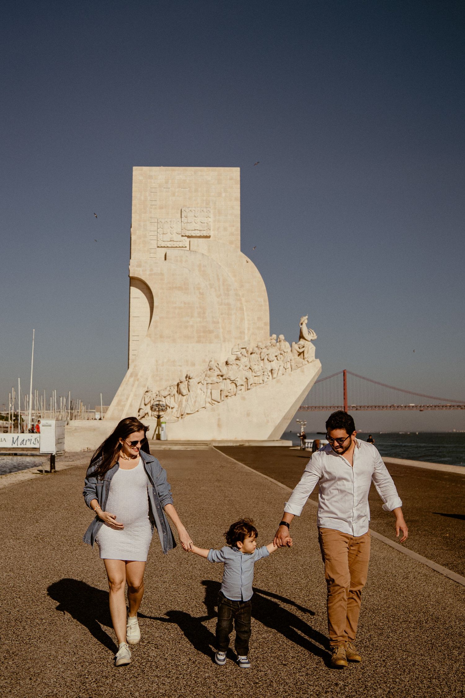 A family holding hands walks along a seaside monument with the Golden Gate Bridge visible in the background.