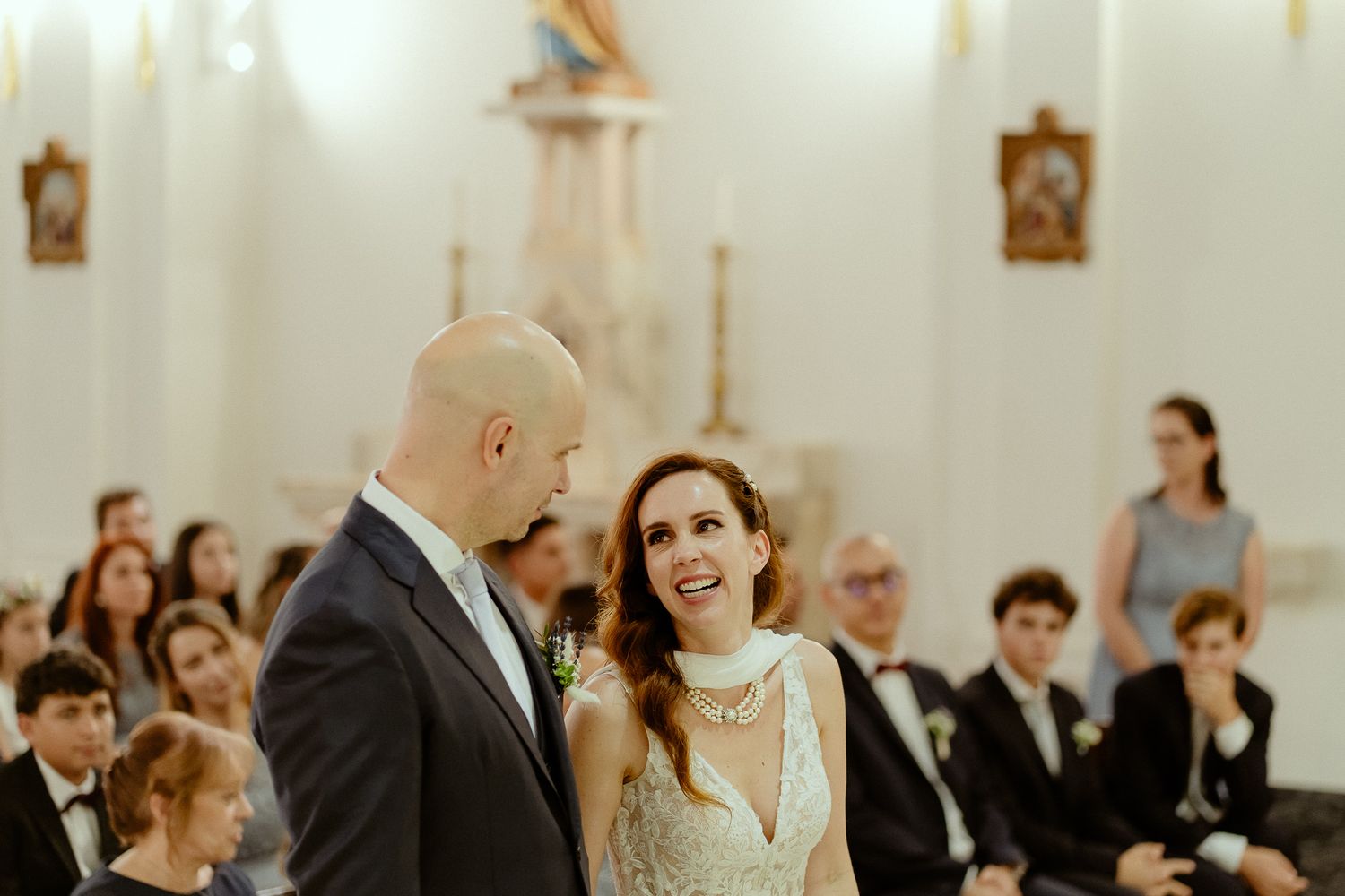 Bride and groom exchange vows at a church wedding ceremony, with guests seated in pews behind them.