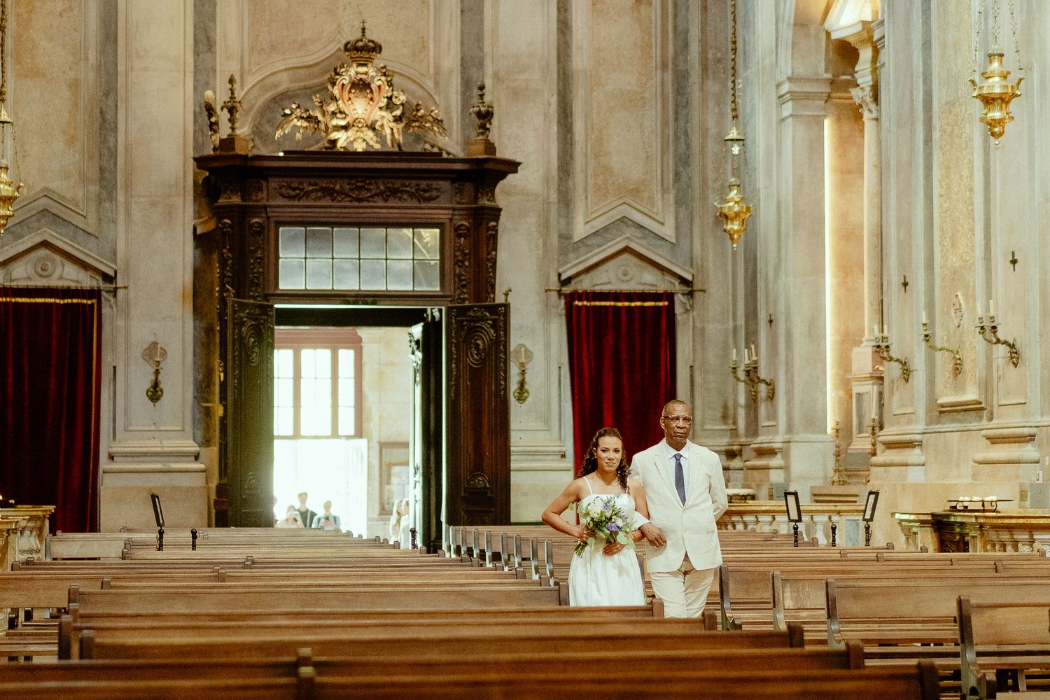 Bride and groom walking down the aisle of an ornate historic church with wooden pews and grand architecture.