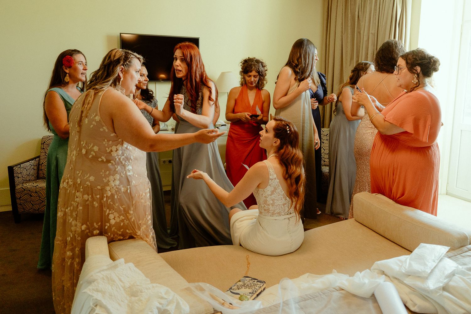 Bridesmaids gather around bride in hotel room during wedding preparations, sharing joyful moments together.
