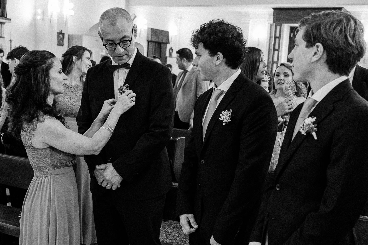 Black and white wedding photo of guests greeting each other warmly inside a church ceremony.