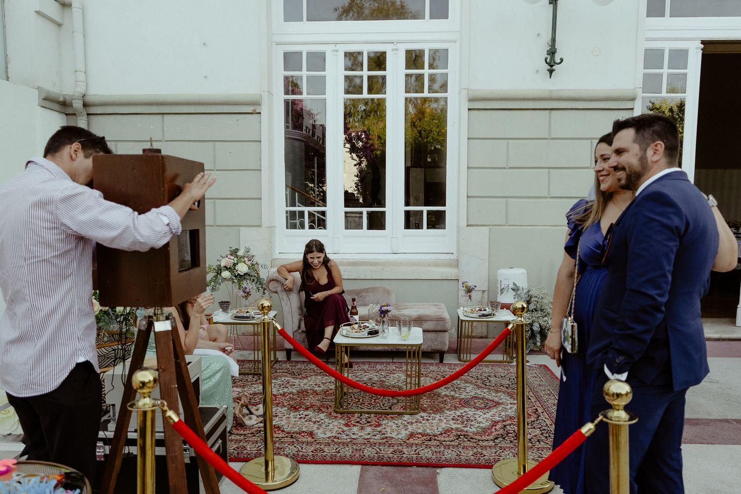 Couple posing for a vintage camera photo booth at an elegant outdoor wedding reception.