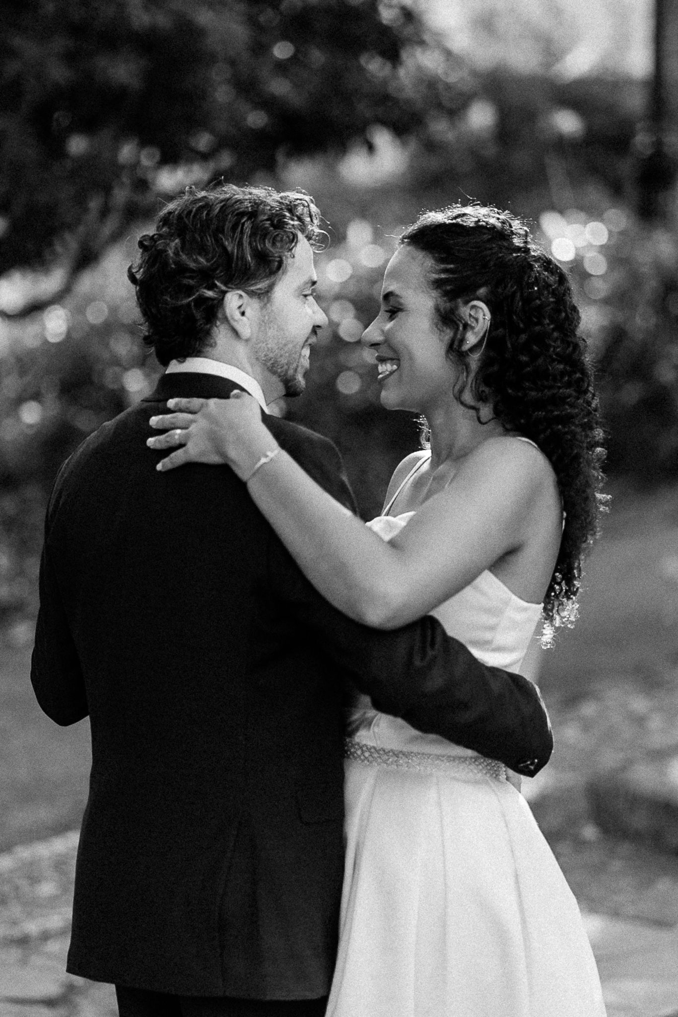Black and white photo of a smiling bride and groom embracing outdoors at their wedding ceremony.