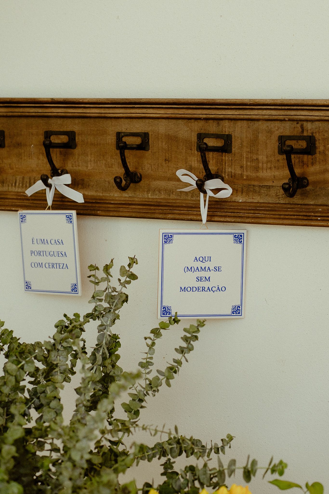 Portuguese wedding decor with tile-inspired signs on wooden coat rack with white ribbon bows and eucalyptus greenery.
