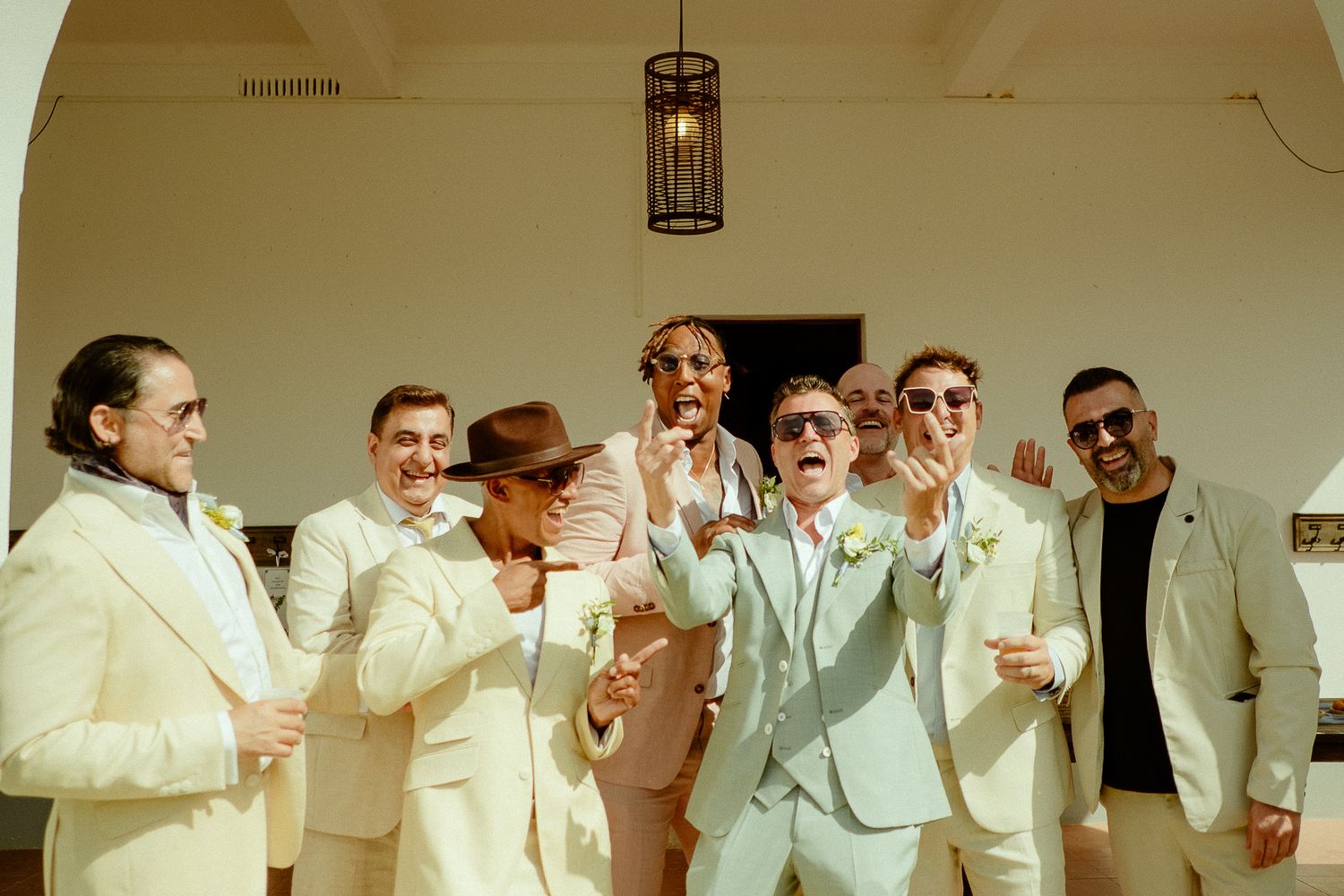 Groom and groomsmen in cream suits laughing and celebrating together at a wedding venue.