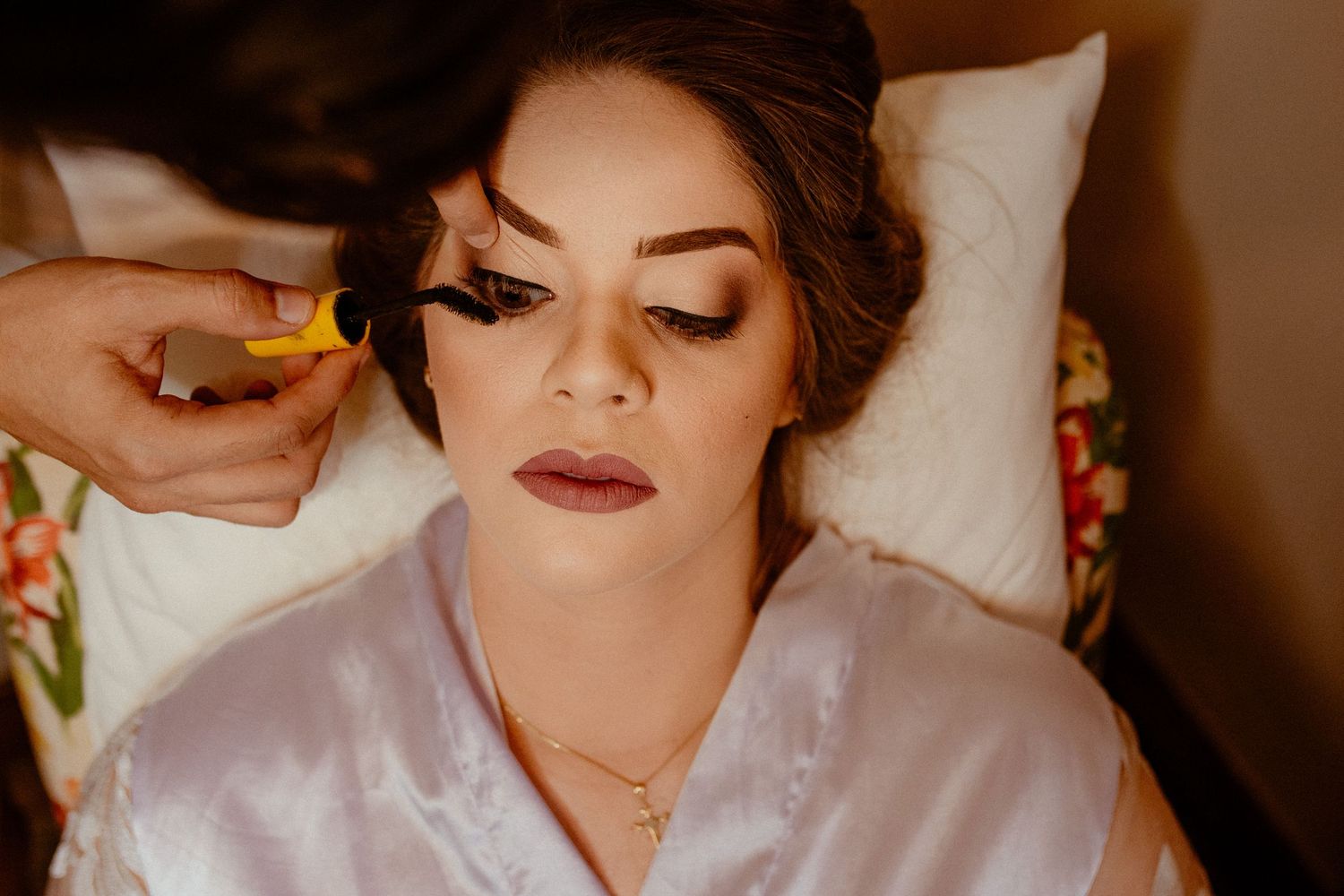 Professional makeup artist applies final touches on a model wearing a white silk robe during a beauty photoshoot.