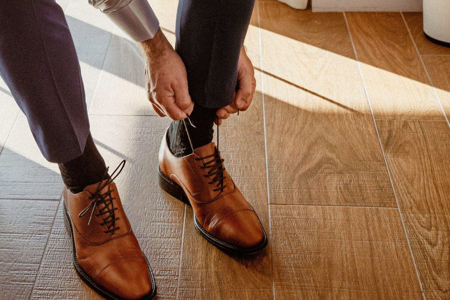 Multiple shots of brown leather dress shoes on a hardwood floor lit by natural sunlight.