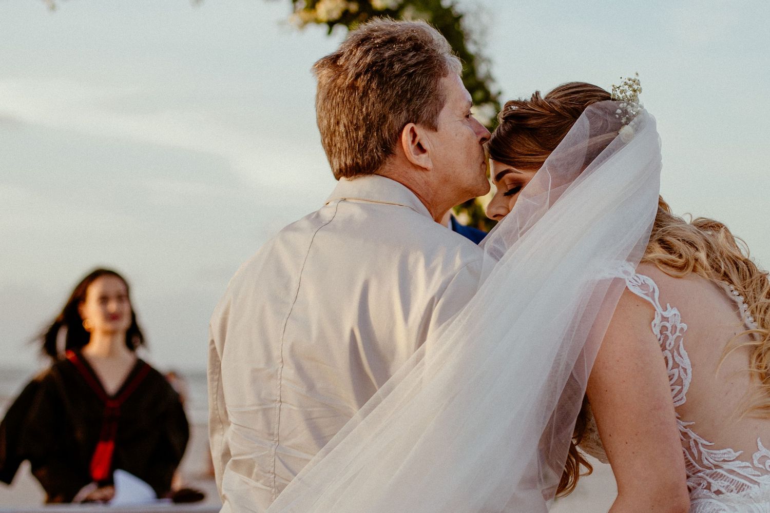 A romantic outdoor beach wedding ceremony as the couple exchanges vows beneath swaying palm trees at sunset.