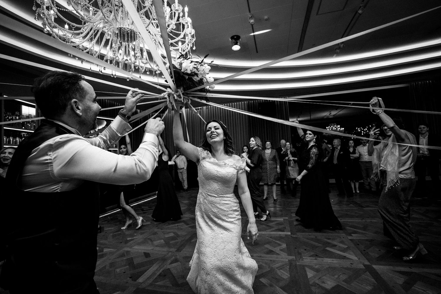 Dynamic black and white shot of wedding celebration under dramatic chandelier lighting.