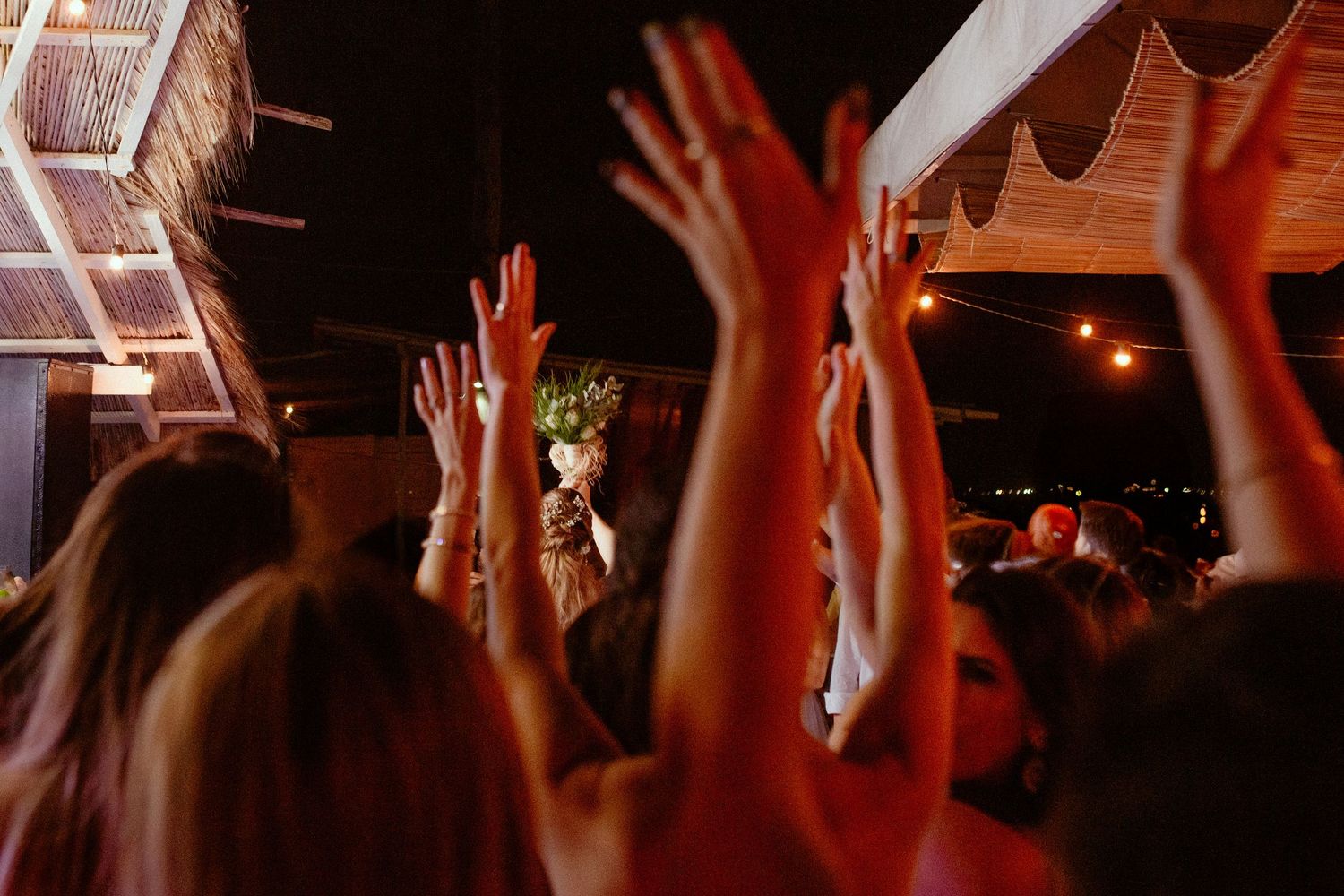 Silhouettes of a crowd with raised hands at a concert with dramatic red lighting effects in the background.