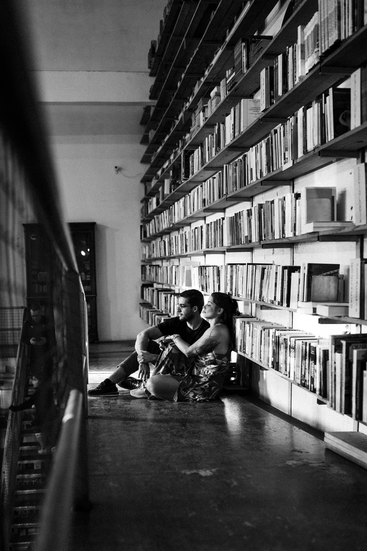 Black and white photo of people reading and studying in the long shelving aisles of an academic library.