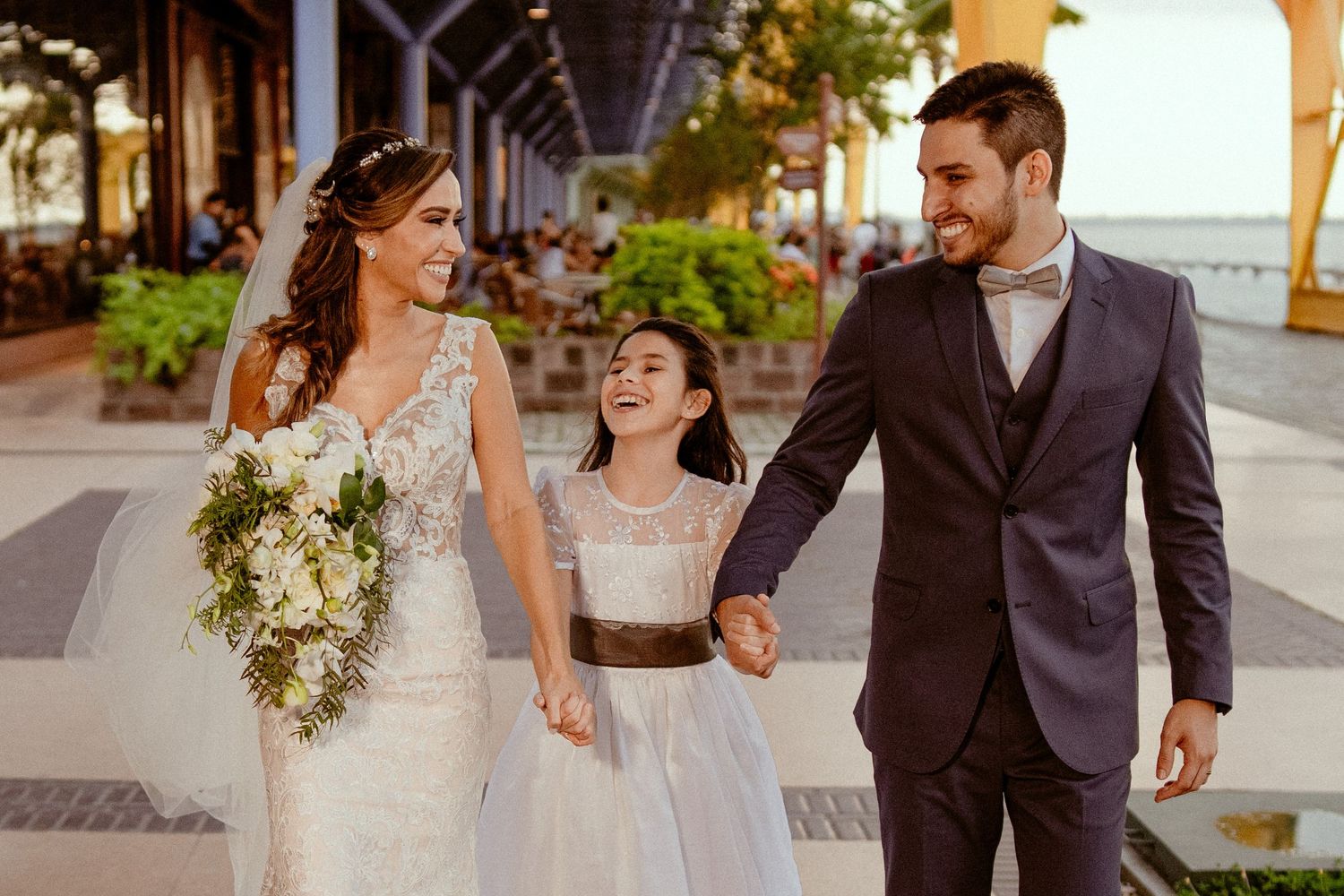 A couple shares a joyful moment walking together in formal wedding attire on a sunny day.