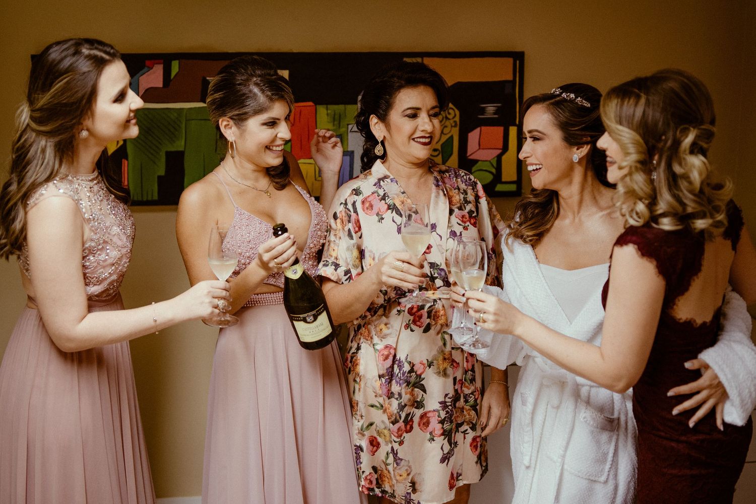 A group celebrating with champagne together while wearing pink bridesmaid dresses and floral robes.