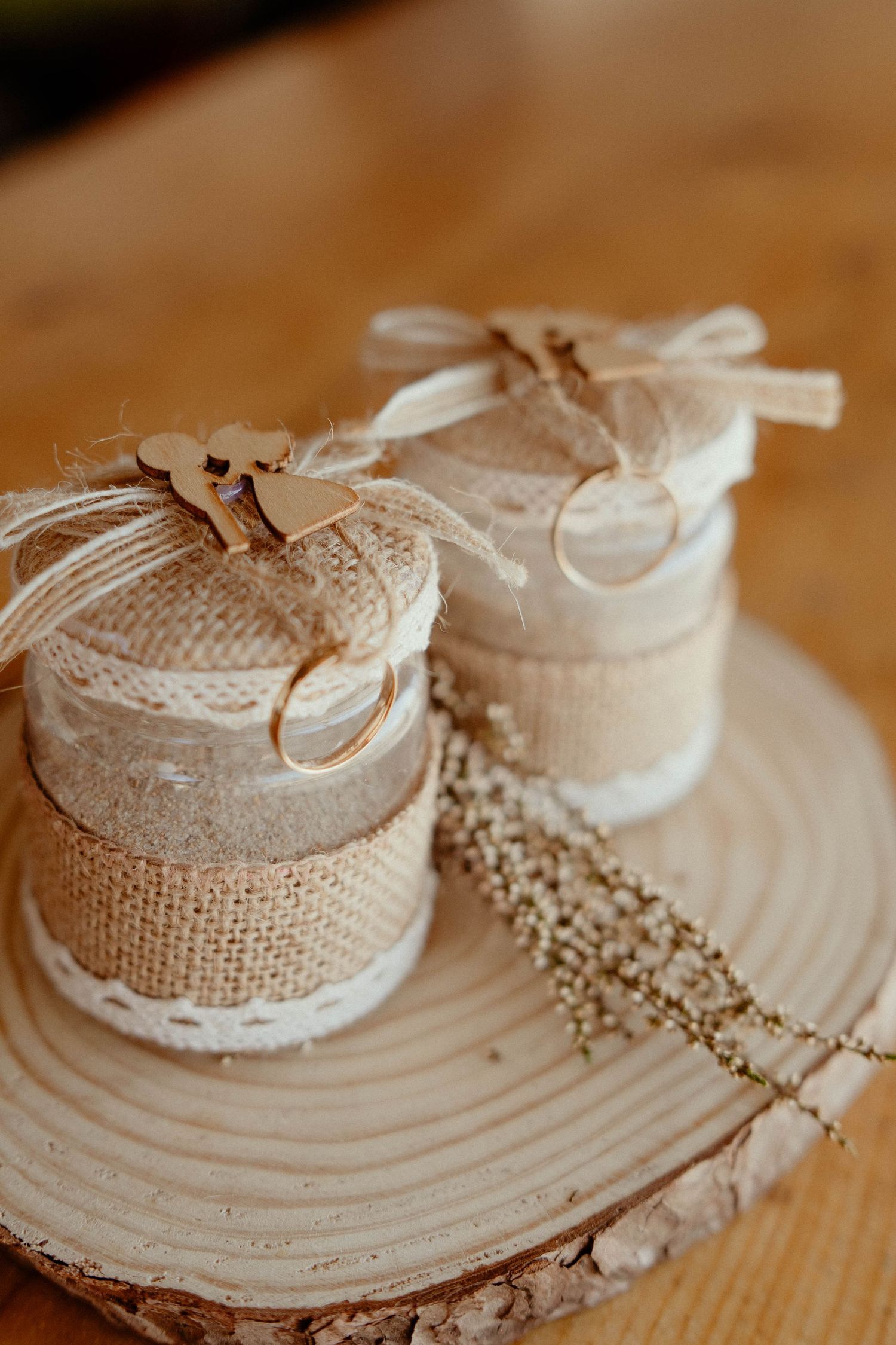 Rustic burlap-wrapped candle holders with delicate lace trim sit on a wooden surface with decorative beaded garland.
