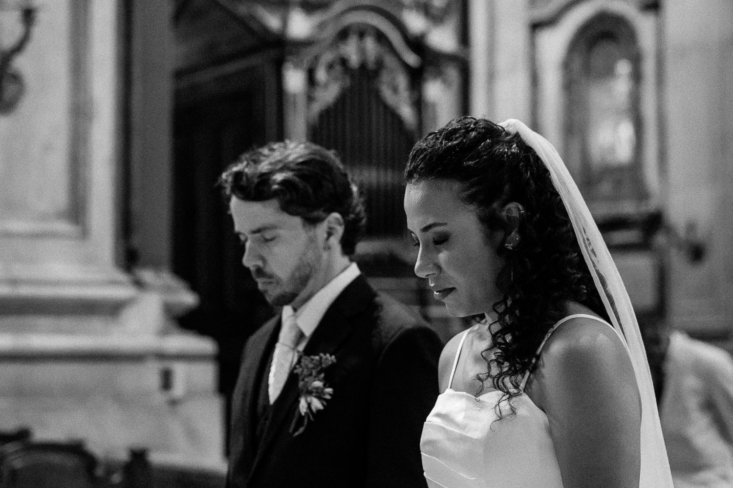 Black and white photo of a bride and groom standing solemnly at the altar during their wedding ceremony.