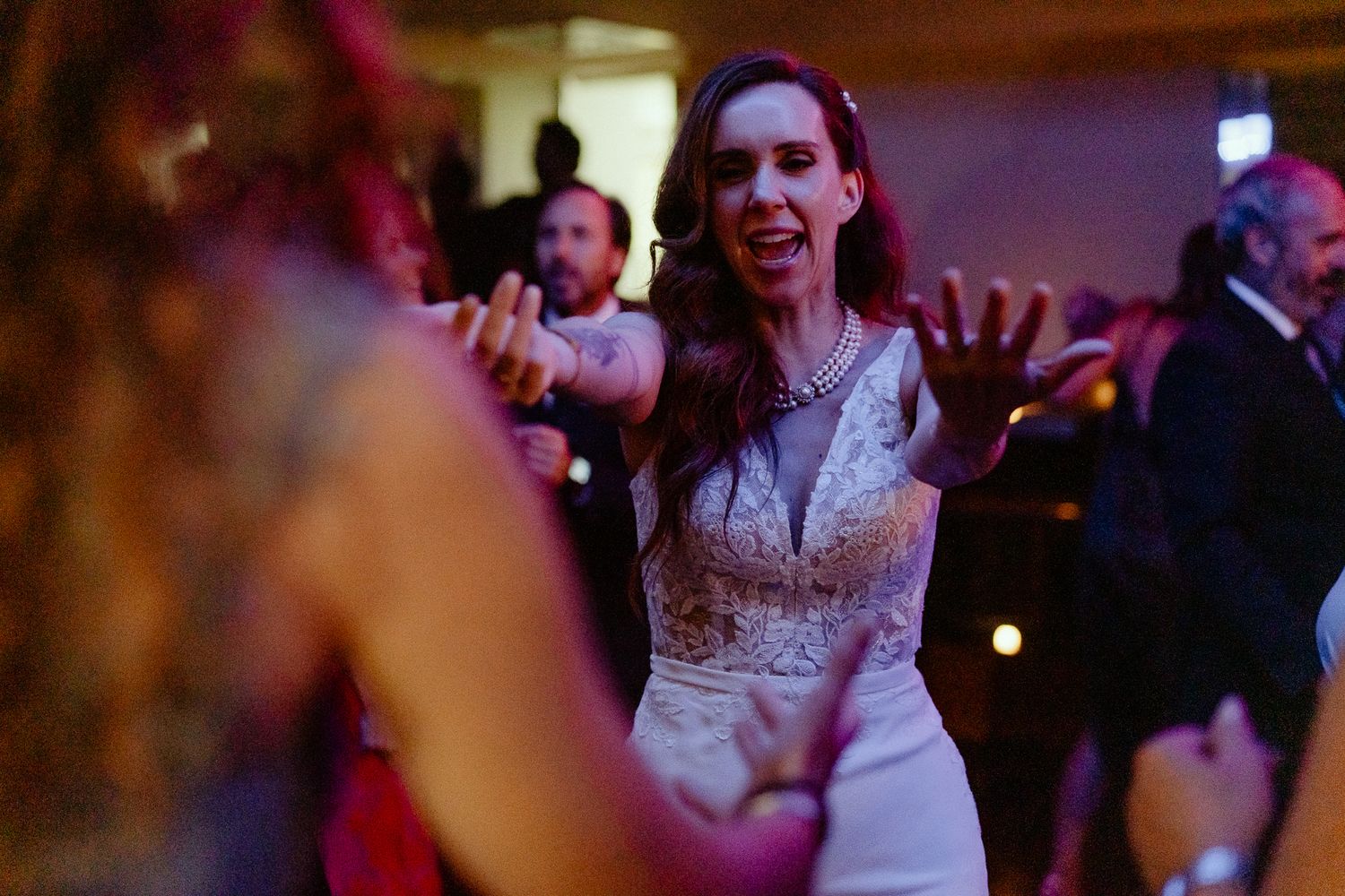 Bride in white lace gown dancing joyfully with guests at elegant wedding reception.