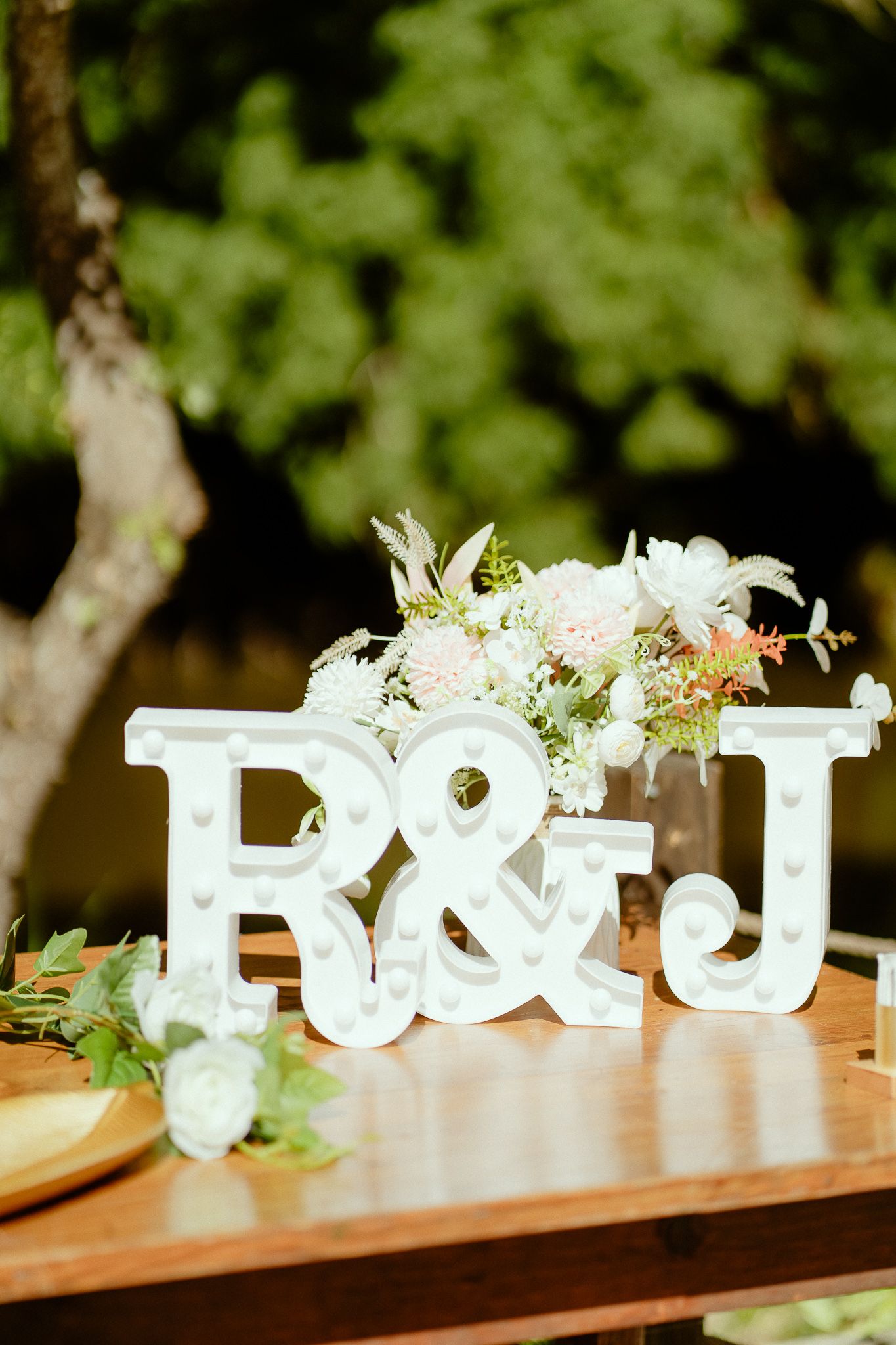 White marquee letter signs R&J on wooden table with floral arrangement, perfect for wedding reception decor.